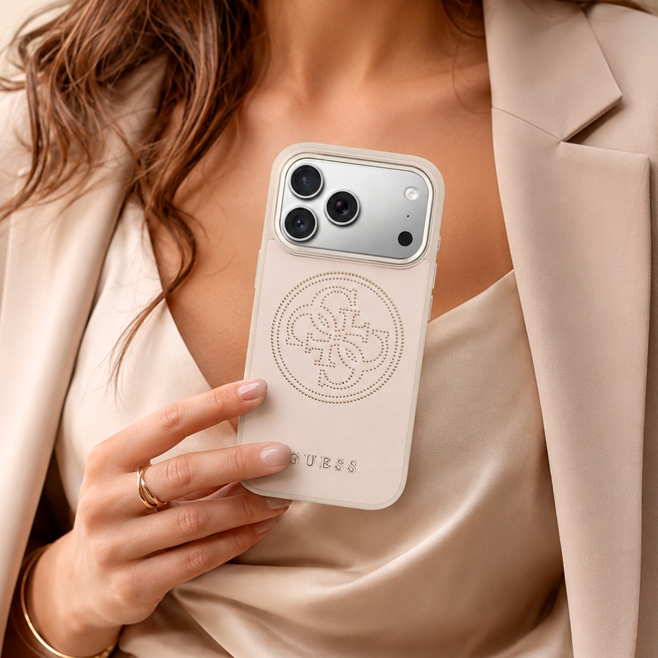 Una persona sostiene una funda beige para iPhone con logo en relieve y la palabra GUESS.