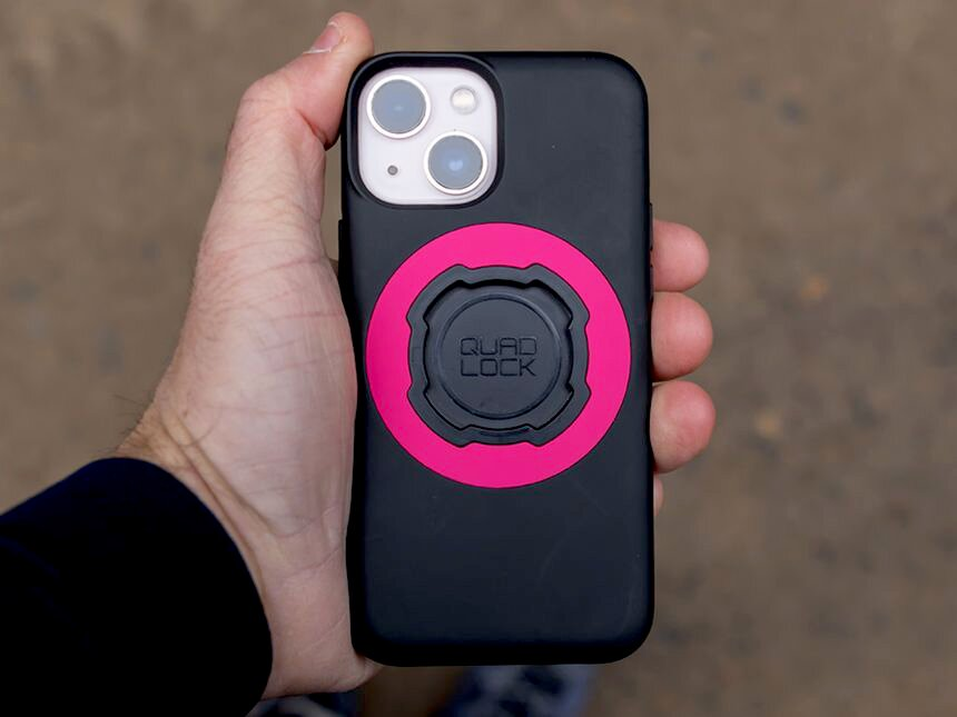 Ein Mann hält ein schwarzes Handy mit pinkem Quad Lock ab. Die Kameras sind oben links.