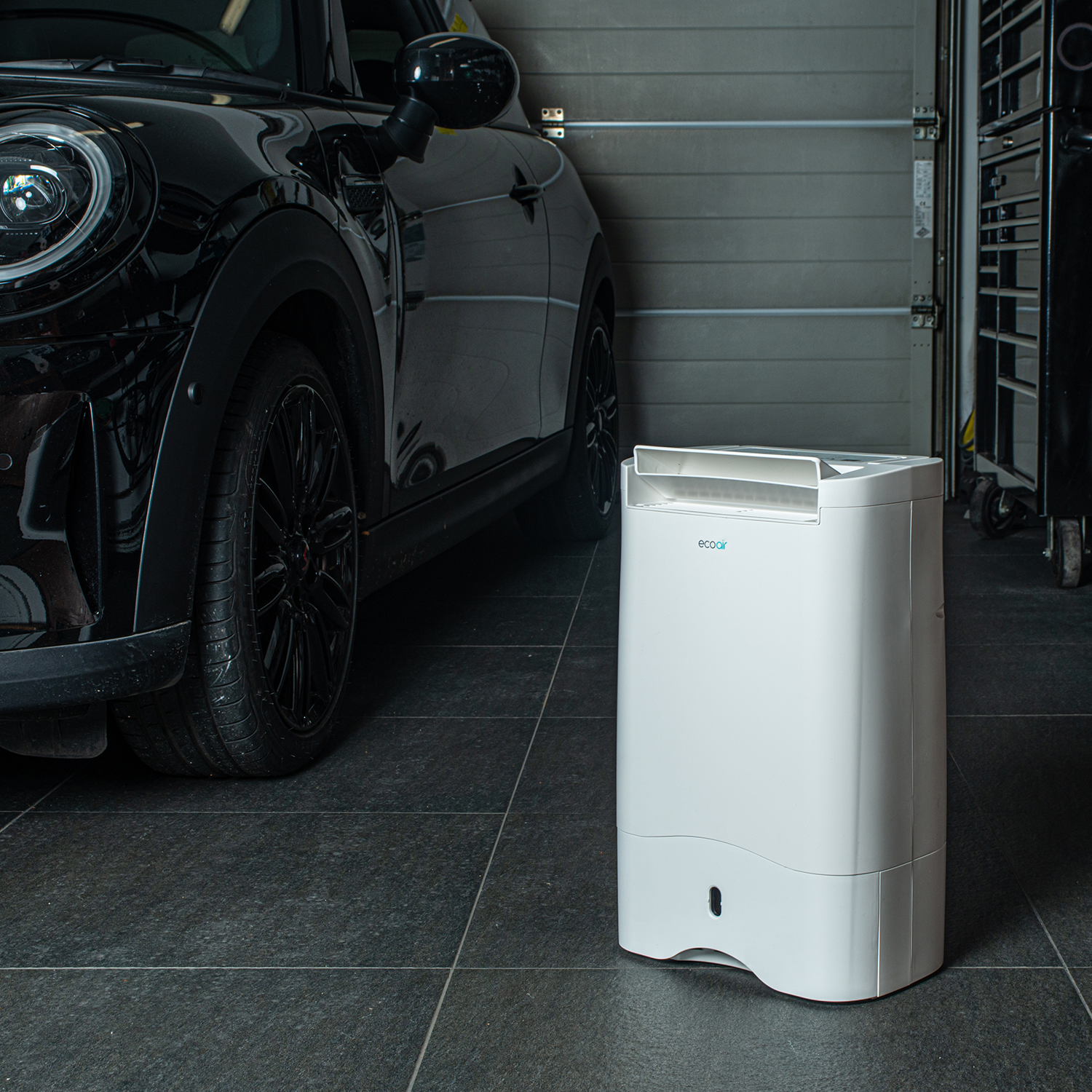 A white dehumidifier sits next to a black car in a garage.