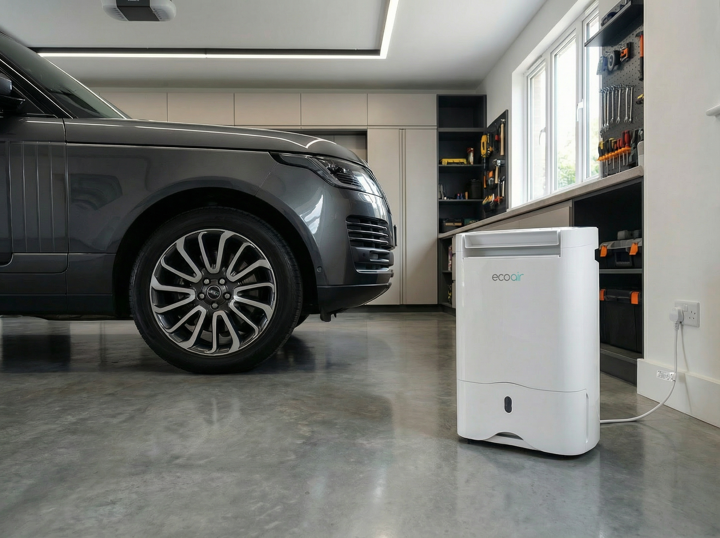 Gray Range Rover next to a white dehumidifier in a garage with a tool wall.