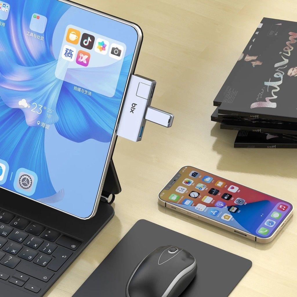 Ahşap bir masada USB-C hub'lı tablet, akıllı telefon, fare ve dergiler.