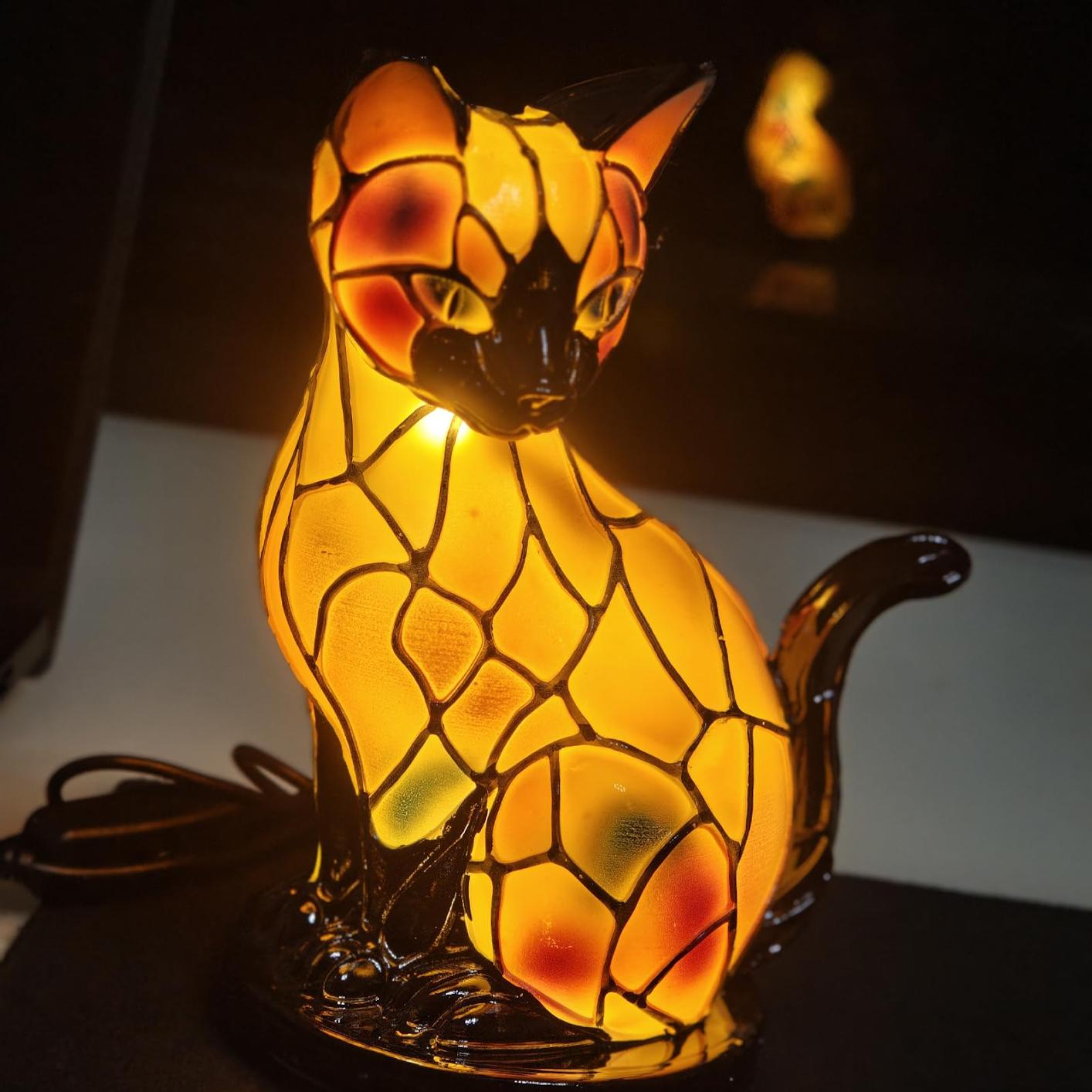 Eine leuchtende Glaslampe in Katzenform mit gelben und roten Glasstücken.