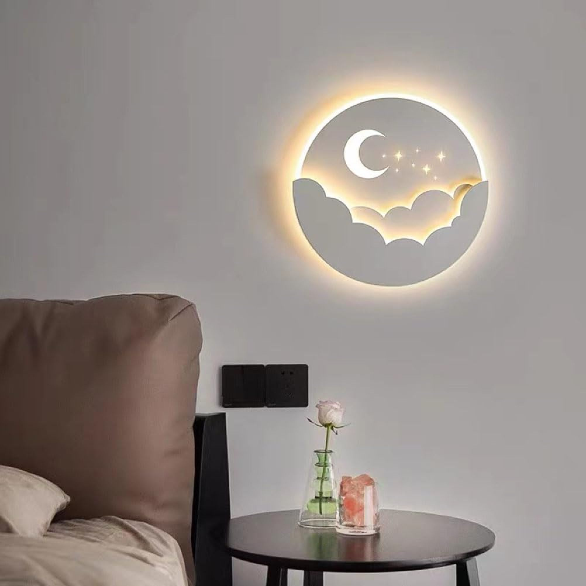 Eine runde Wandleuchte mit Mond und Sternen über Wolken, beleuchtet ein Schlafzimmer.