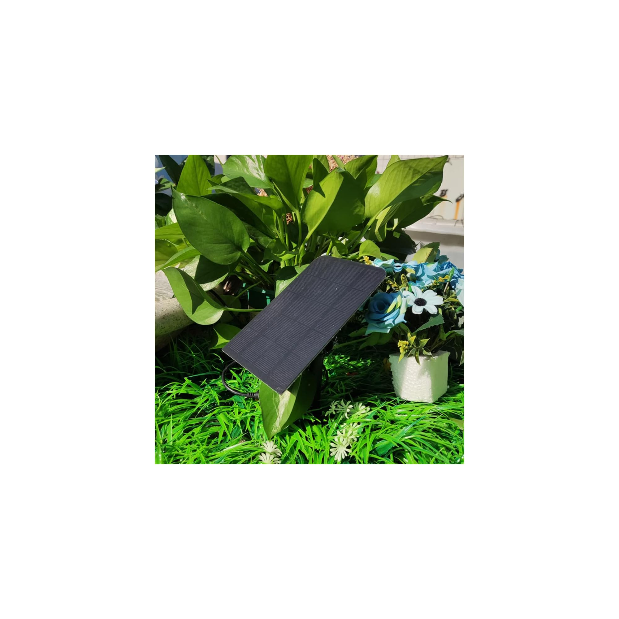 Ein kleines Solarpanel steht vor grünen Pflanzen und blau-weißen Blumen.