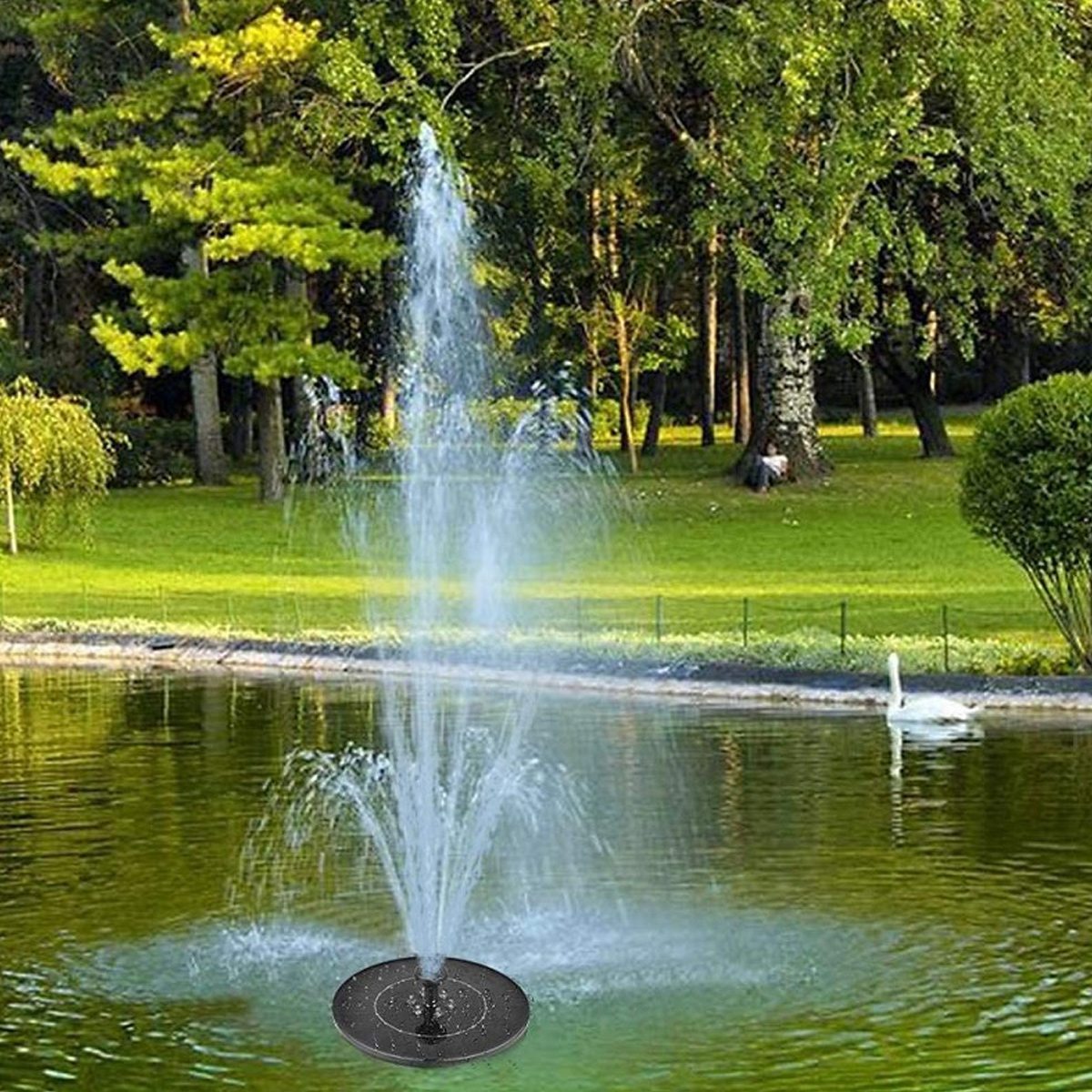 Ein Solarbrunnen sprüht Wasser in einen Teich, mit Bäumen und einem Schwan im Hintergrund.