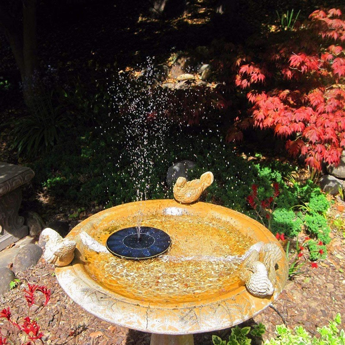 Ein Vogelbad mit einem Solarbrunnen und Vogeldekorationen in einem Garten.