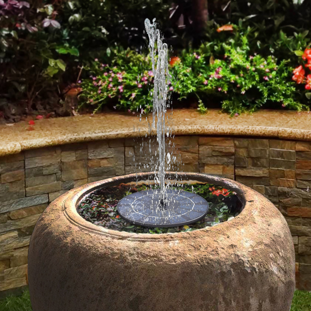 Ein Solarbrunnen sprüht Wasser in einem Terrakotta-Topf vor blühenden Pflanzen.