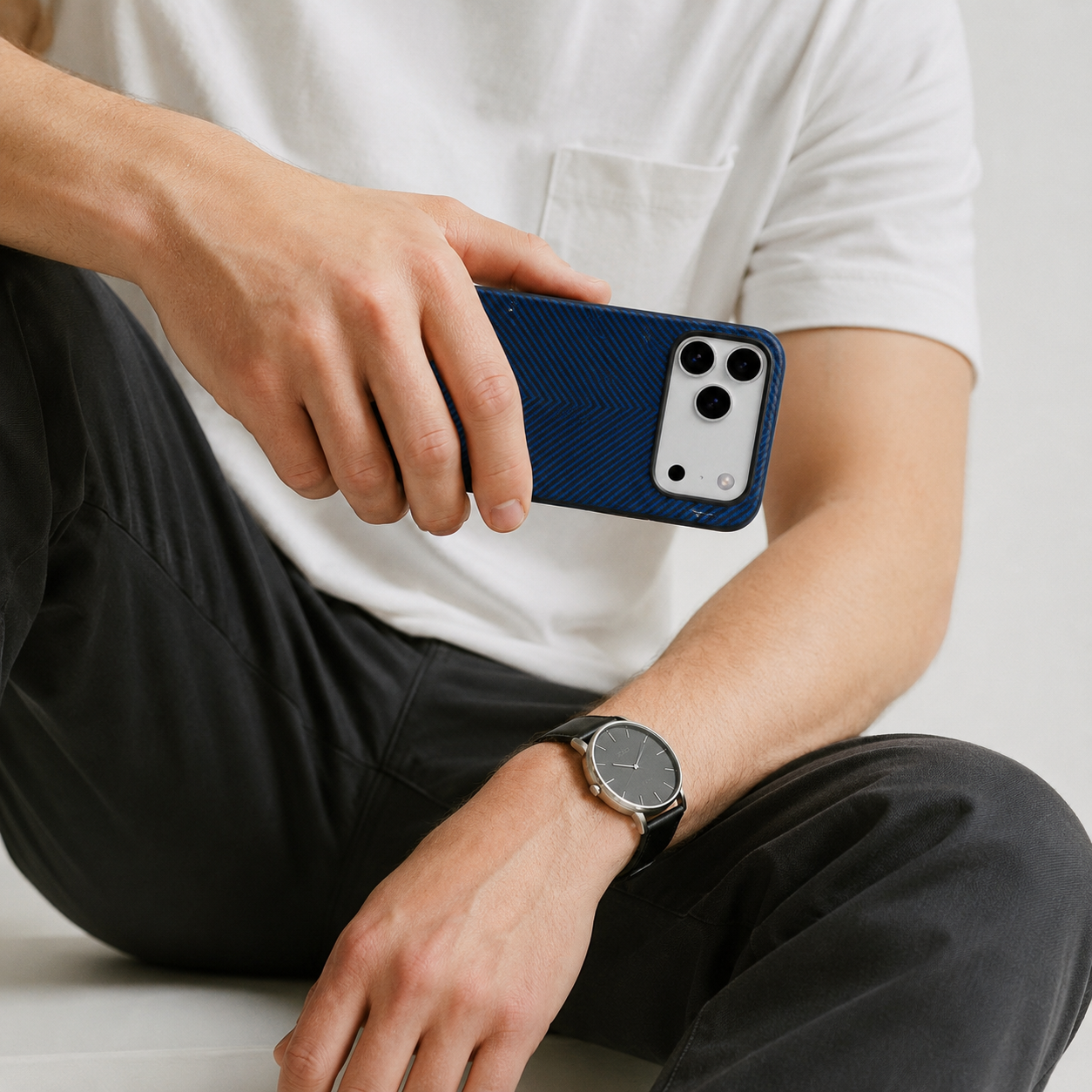 Hombre con funda azul, camiseta blanca, pantalones negros, reloj.