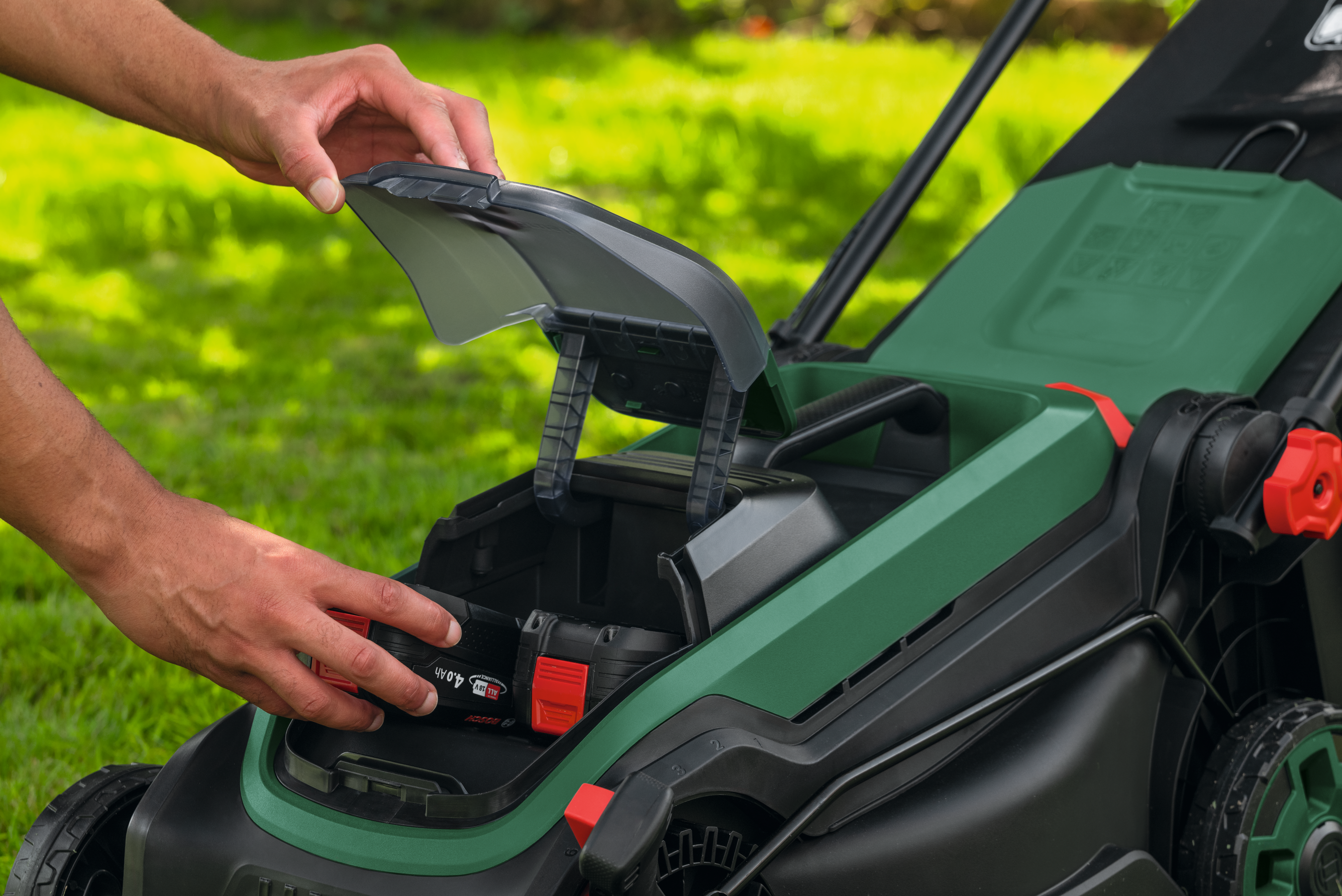 Eine Hand setzt eine grüne Batterie in einen Rasenmäher ein.
