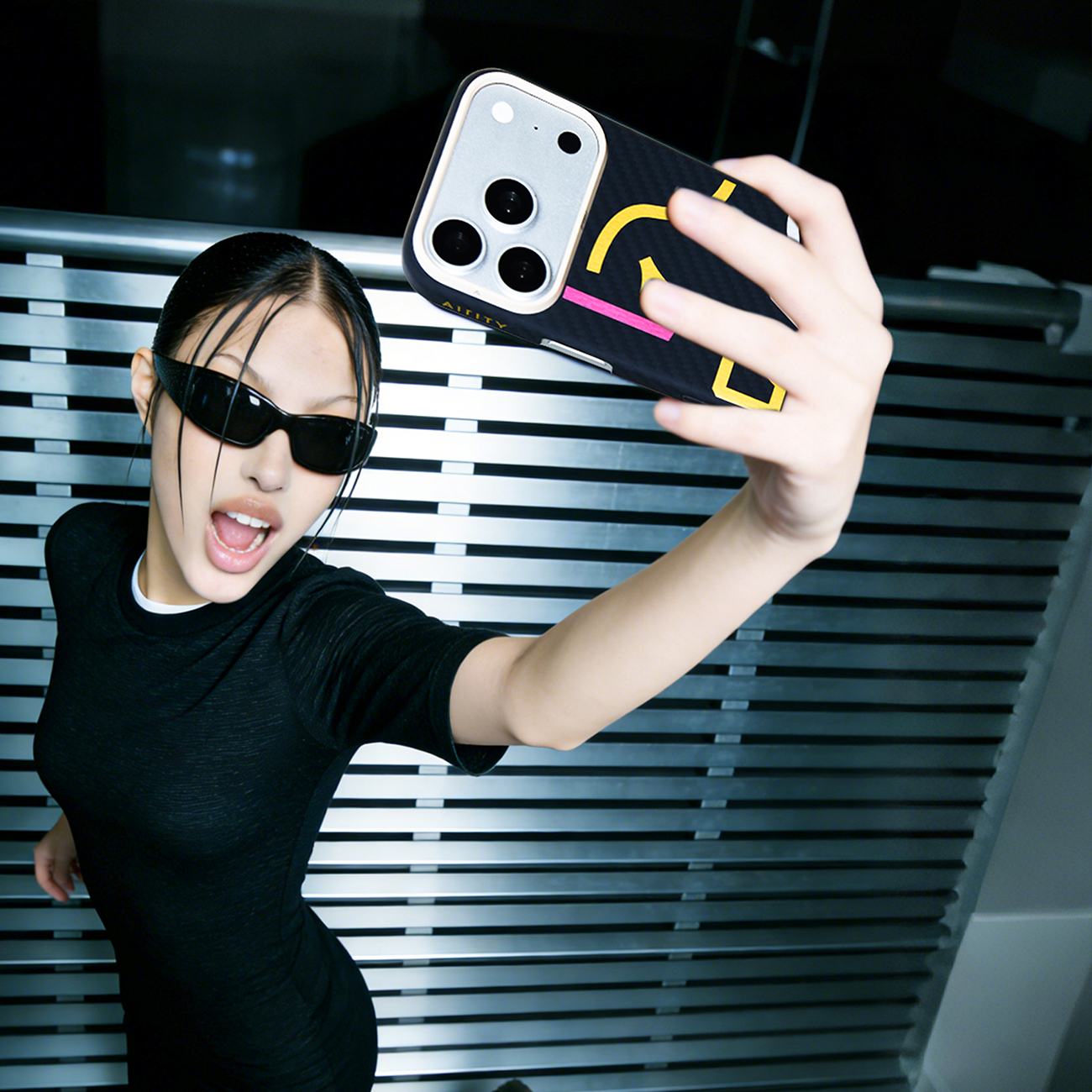 Mujer joven con gafas de sol se toma un selfie con un teléfono de patrón colorido.