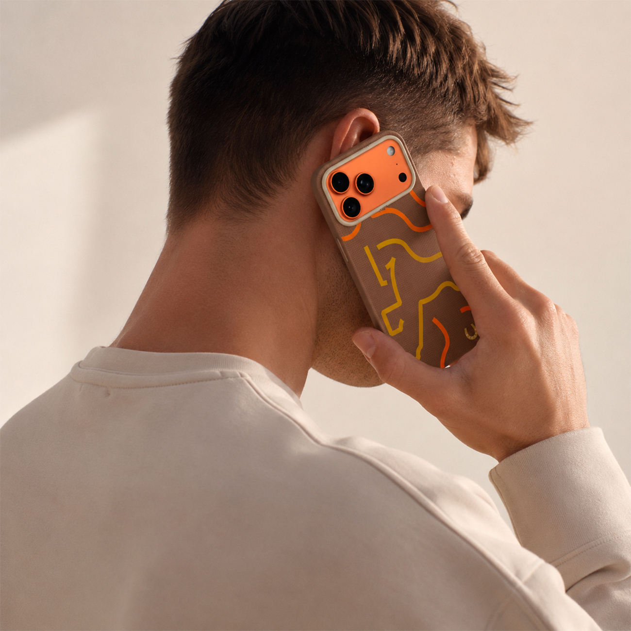 Hombre en el teléfono con funda de patrón marrón, carcasa de cámara naranja.