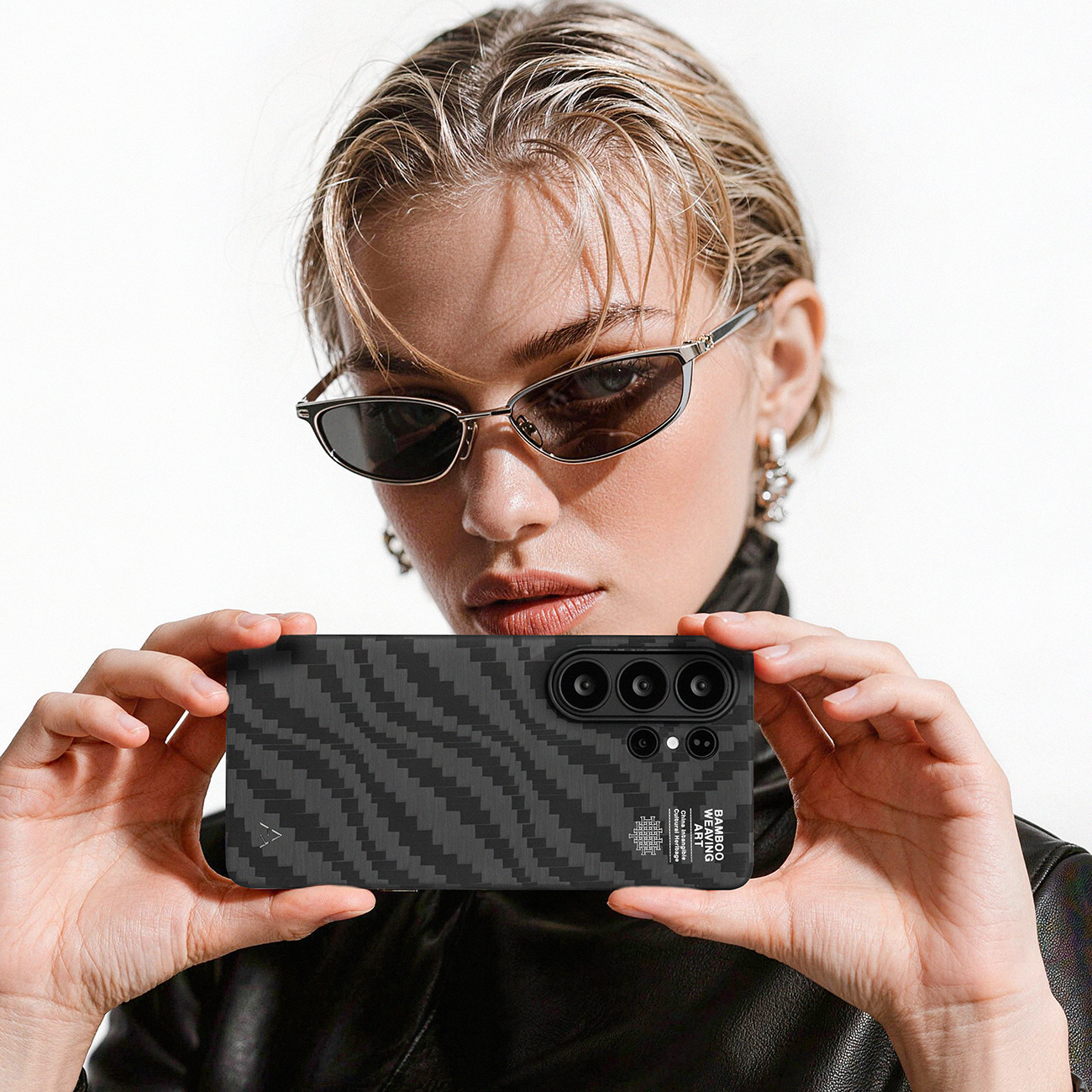 Una mujer con gafas de sol sostiene un smartphone con funda de fibra de carbono.
