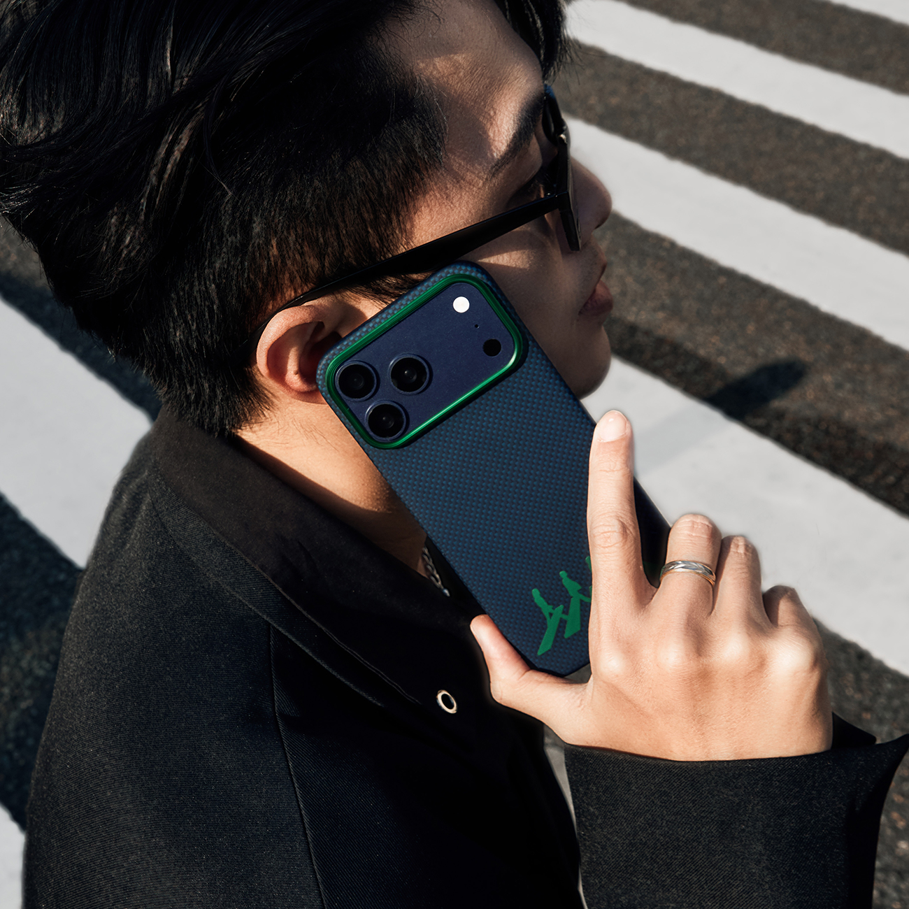 Hombre hablando por teléfono con funda oscura y borde verde en paso de cebra.