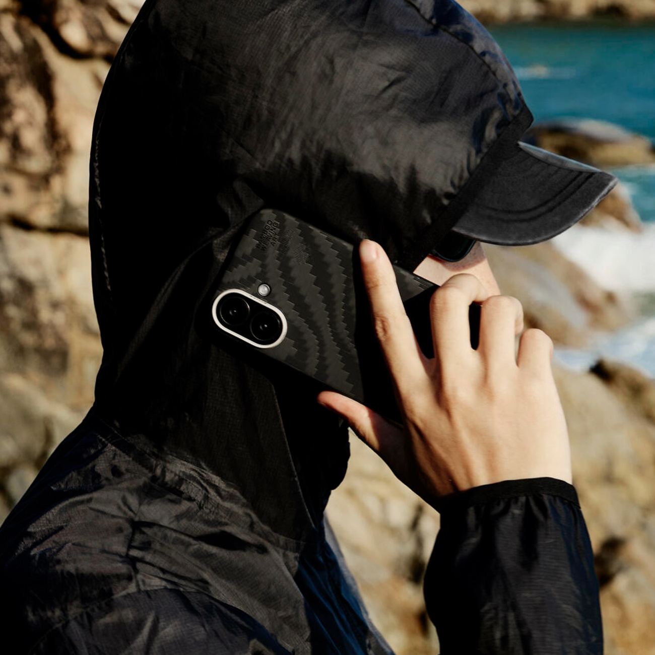 Persona con capucha habla por teléfono con funda de carbono al aire libre.