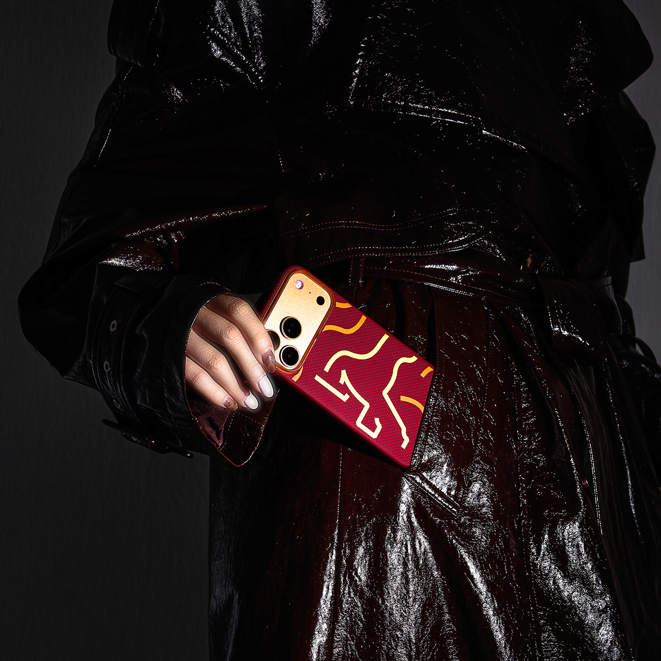 Persona con abrigo brillante sosteniendo un smartphone con funda roja y patrón amarillo.