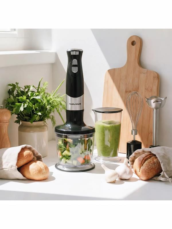 Doğranmış sebzeler, yeşil smoothie bardağı, ekmek ve sarımsak içeren siyah el blenderı.