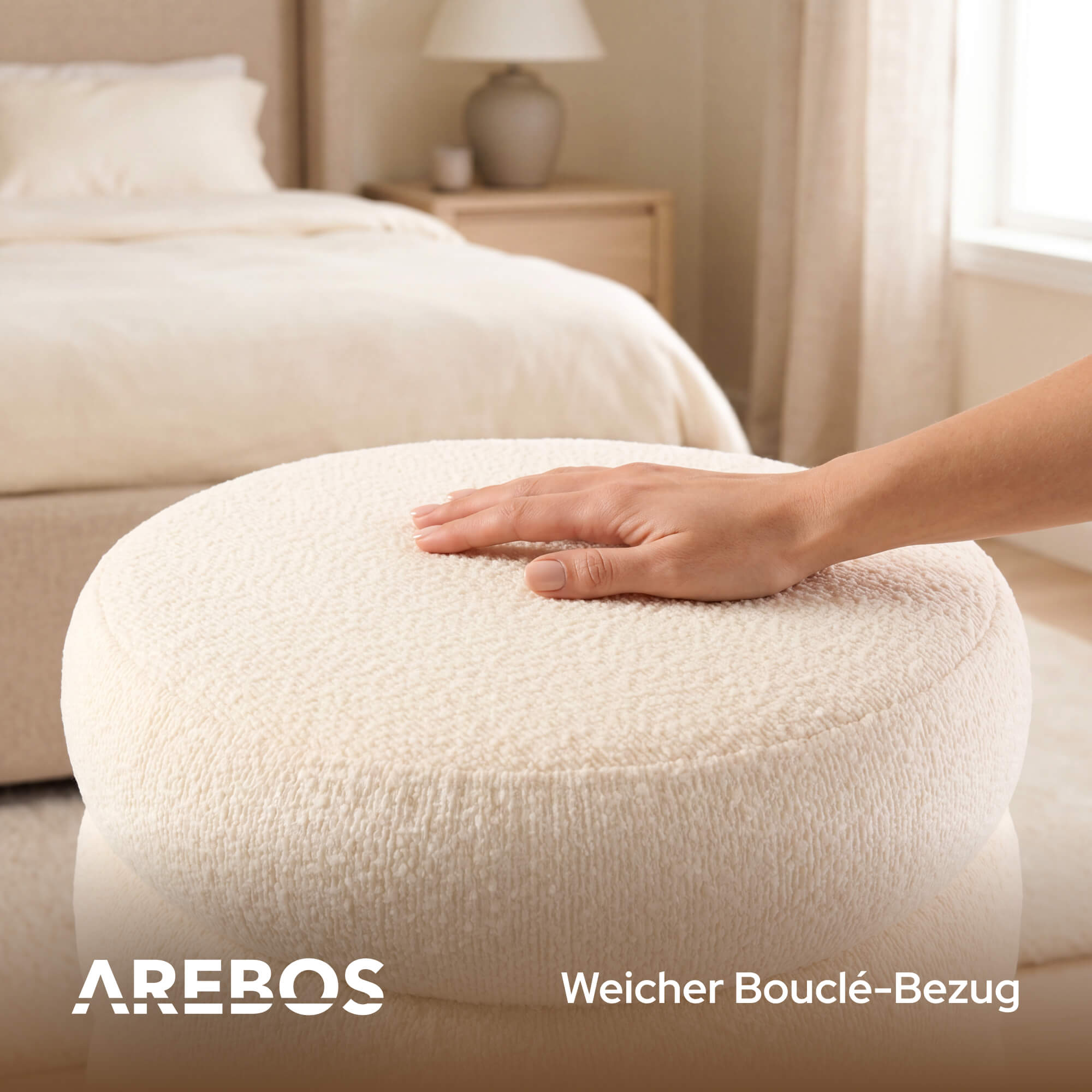 Eine Hand ruht auf einem cremefarbenen Hocker im Schlafzimmer mit Bett und Nachttisch.