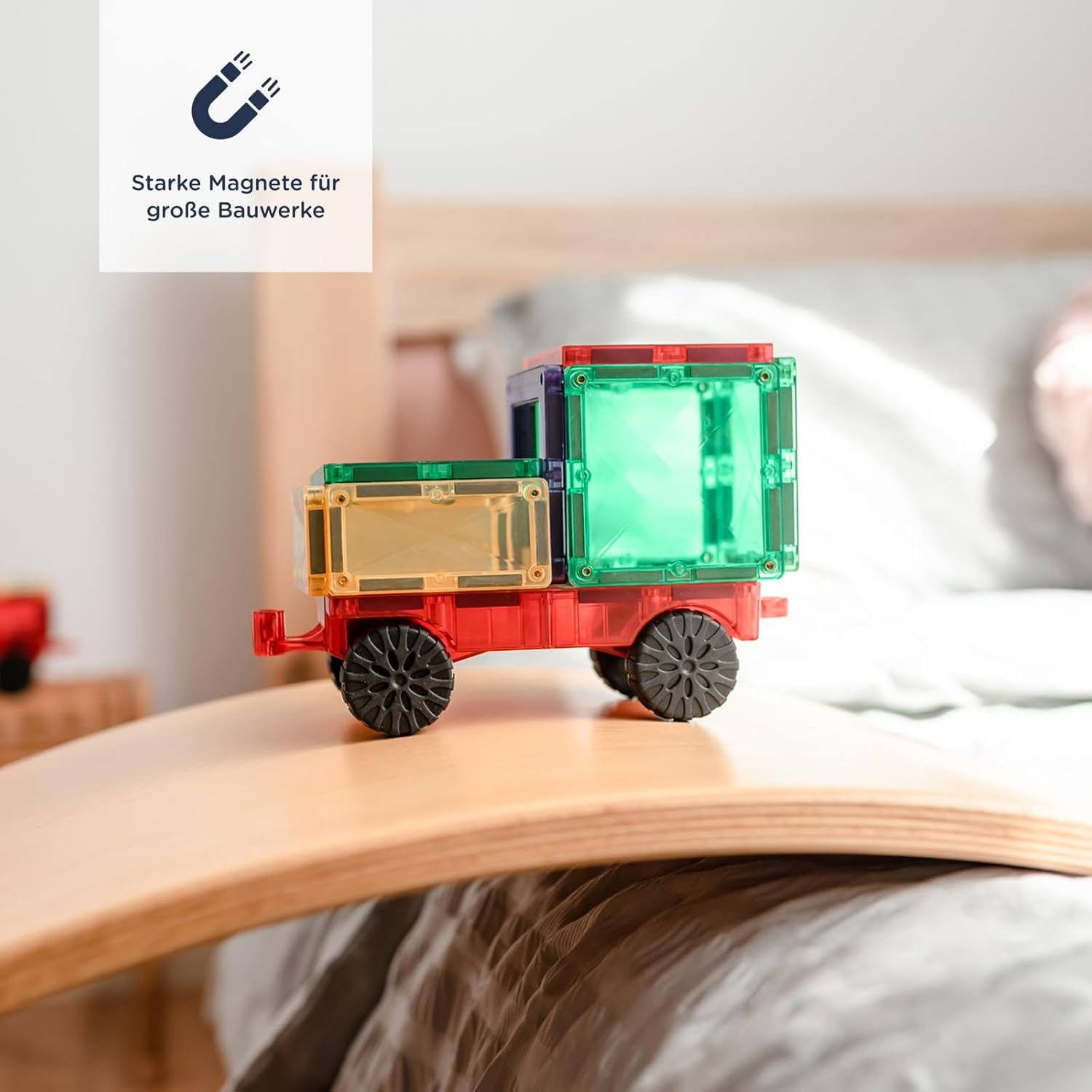 Un camion giocattolo magnetico colorato con ruote nere su una tavola da gioco in legno.