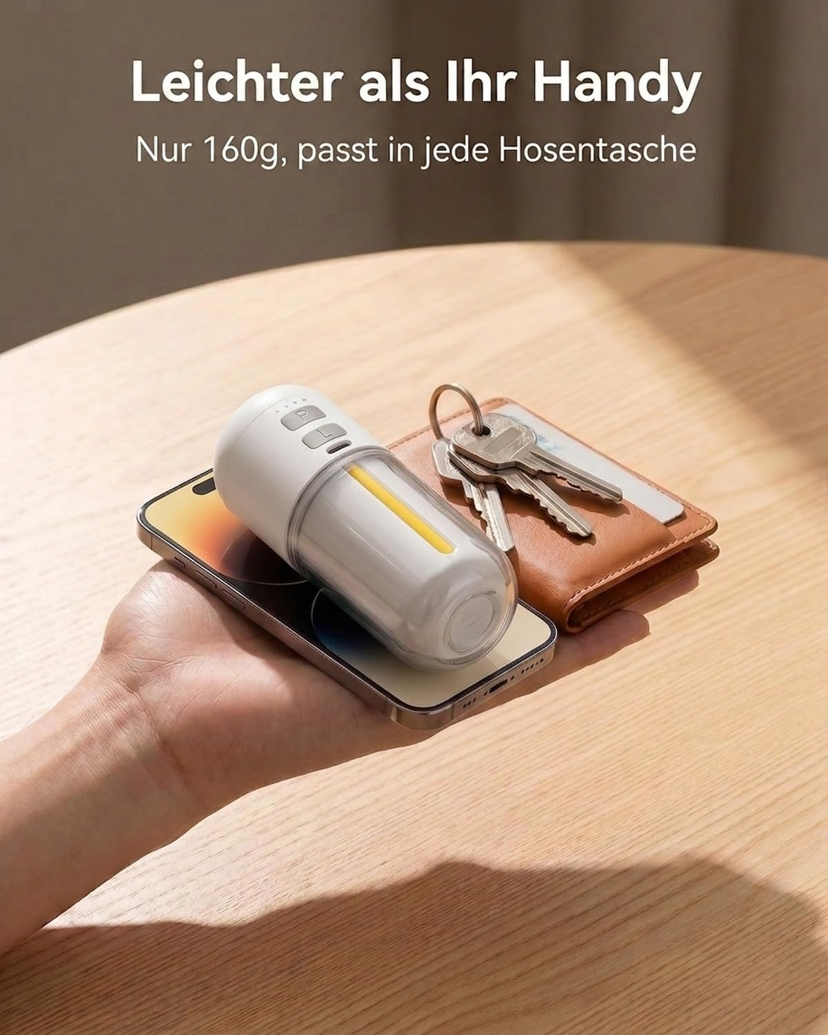 Ein weißer Behälter mit gelbem Streifen liegt auf einem Handy. Schlüssel und Portemonnaie liegen daneben.