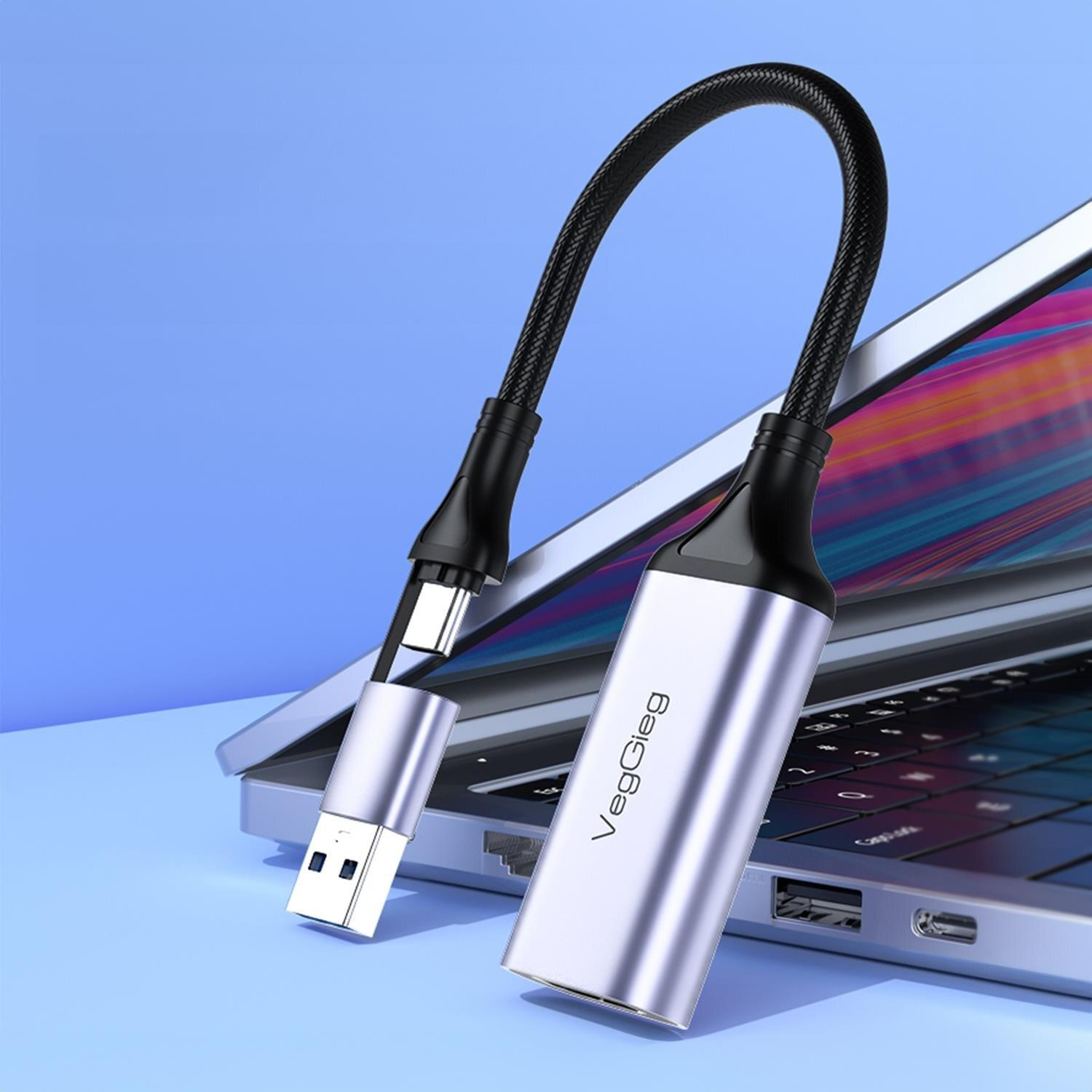 Gümüş USB-C adaptör, siyah kablo ve USB fişiyle dizüstü bilgisayar üzerinde.
