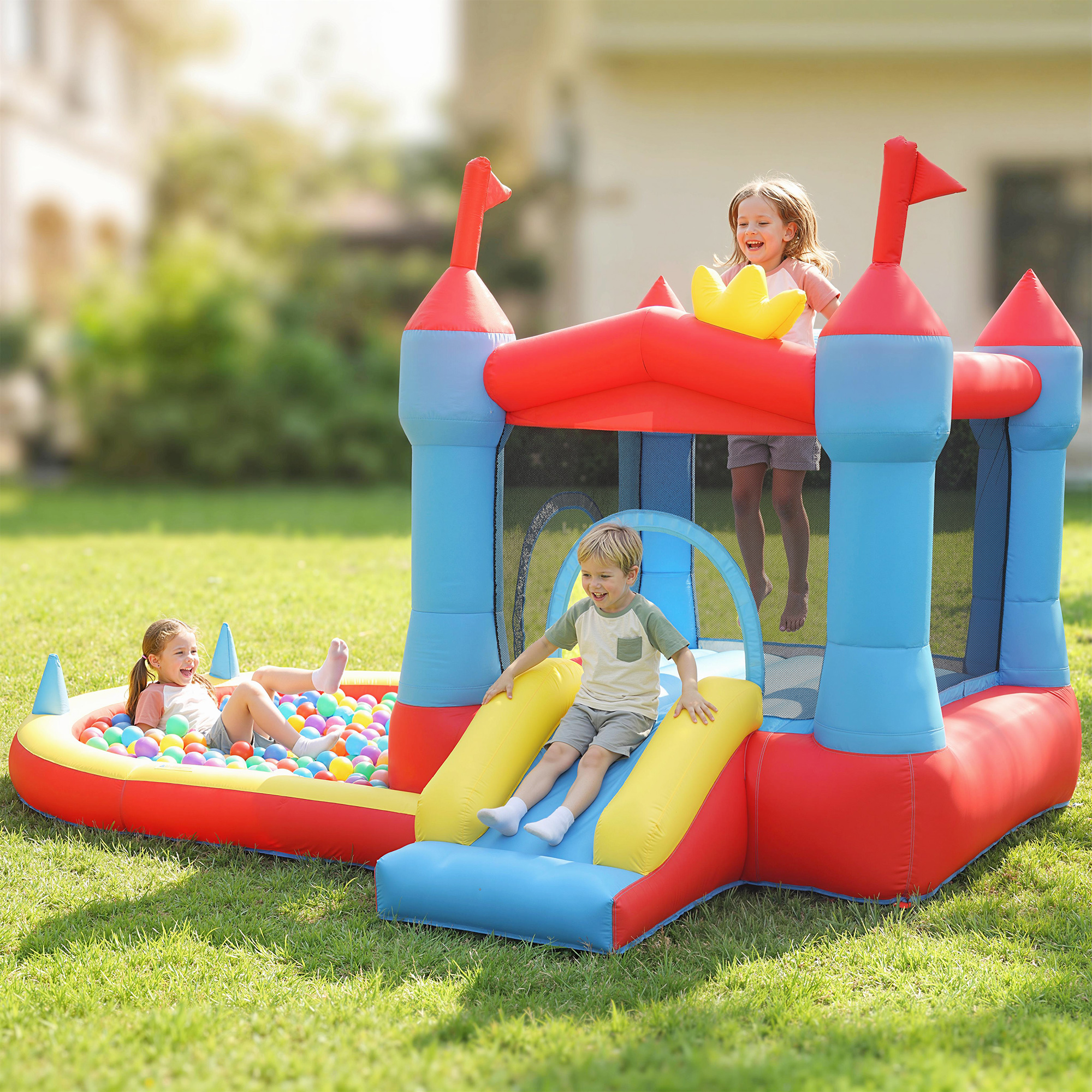 Bambini giocano su un castello gonfiabile con scivolo e piscina di palline in cortile.