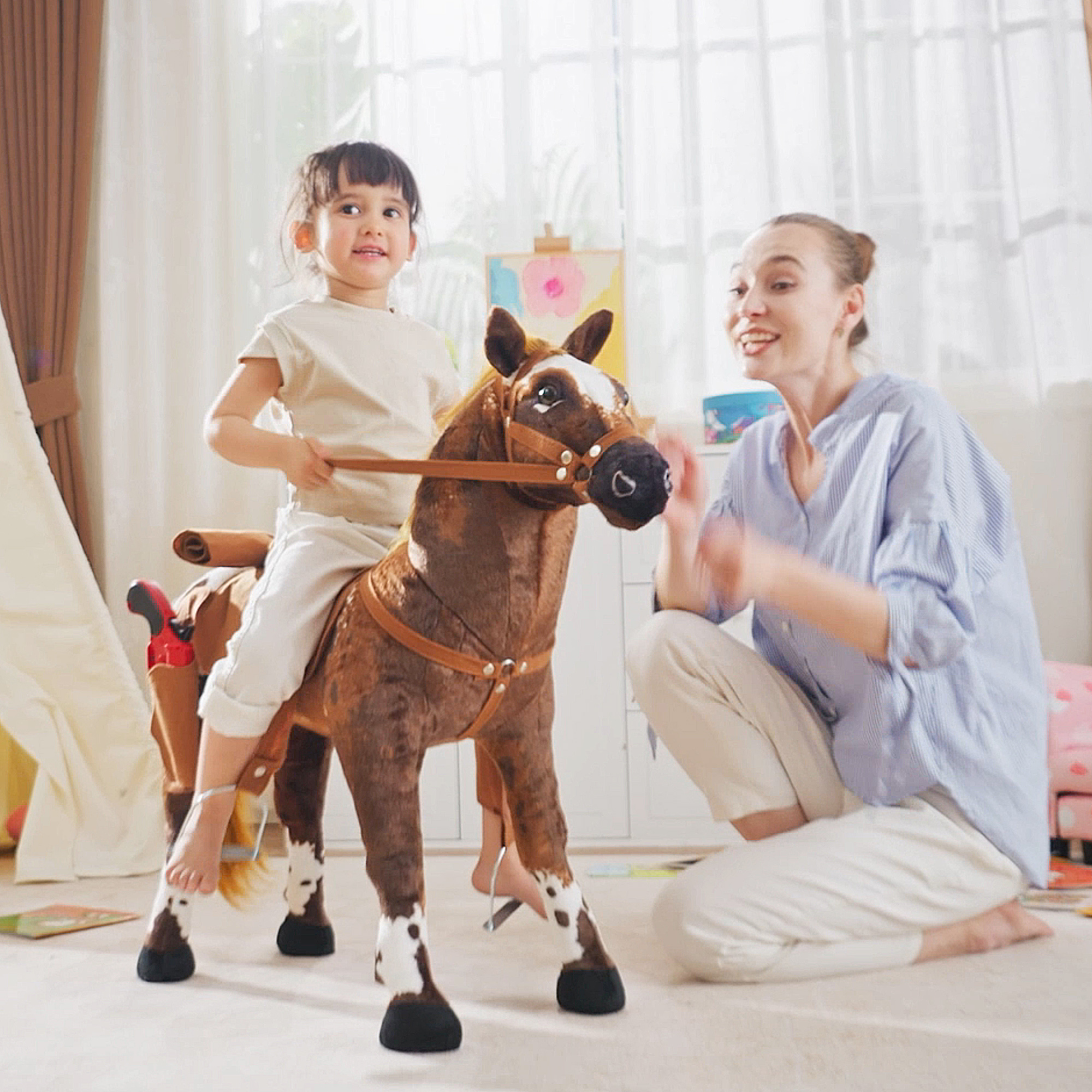 Una bambina cavalca un cavallo giocattolo mentre una donna è inginocchiata accanto.