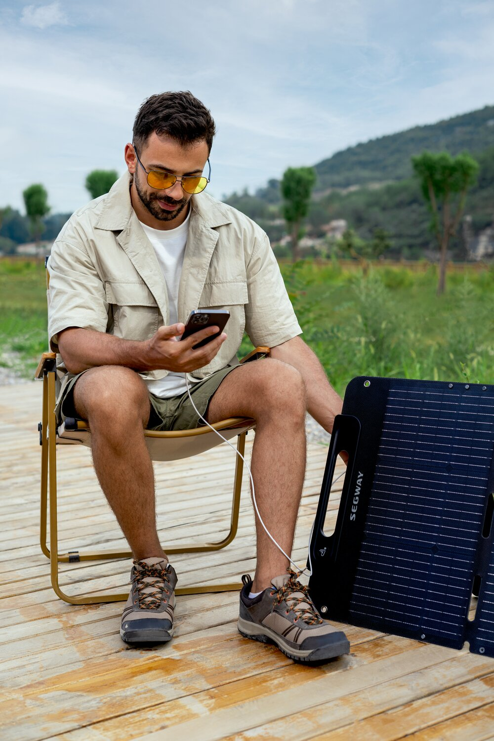 Ein Mann sitzt auf einem Stuhl und benutzt sein Handy, das an ein Solarpanel angeschlossen ist.