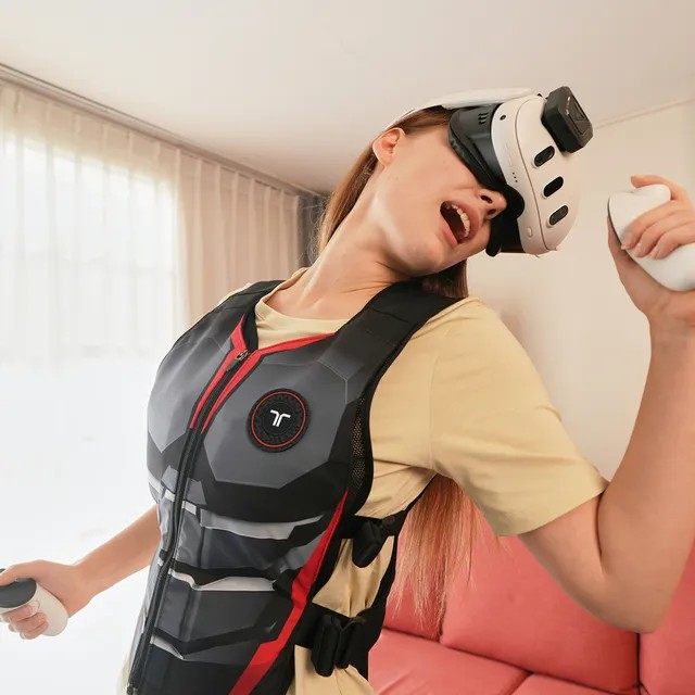 Mujer con gafas VR y chaleco sostiene mandos, cantando.