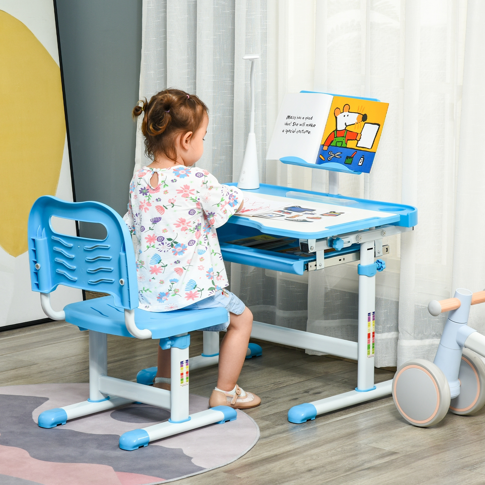 Una bambina siede a una scrivania blu leggendo un libro.