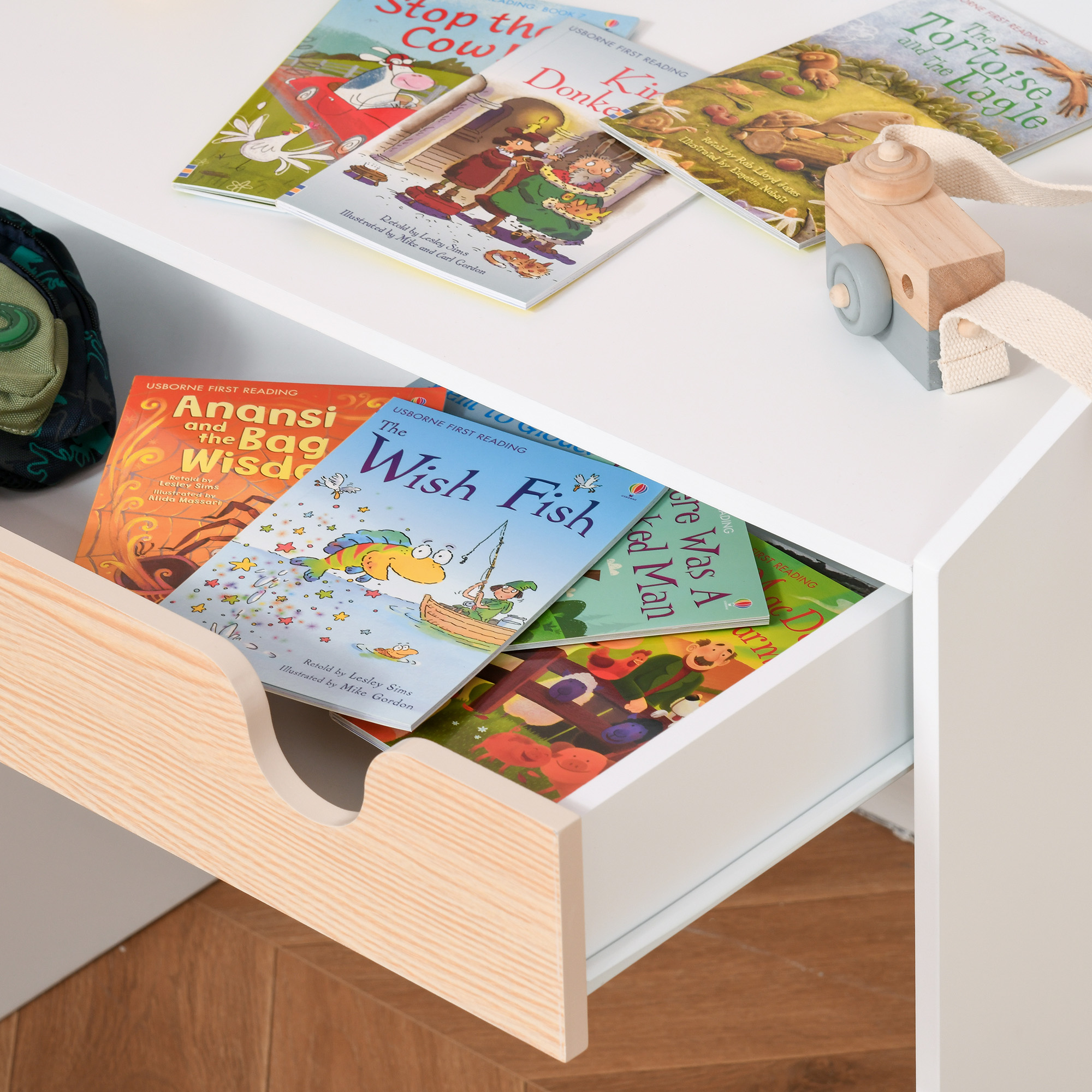 Una mensola bianca con libri per bambini e una macchina fotografica giocattolo in legno.
