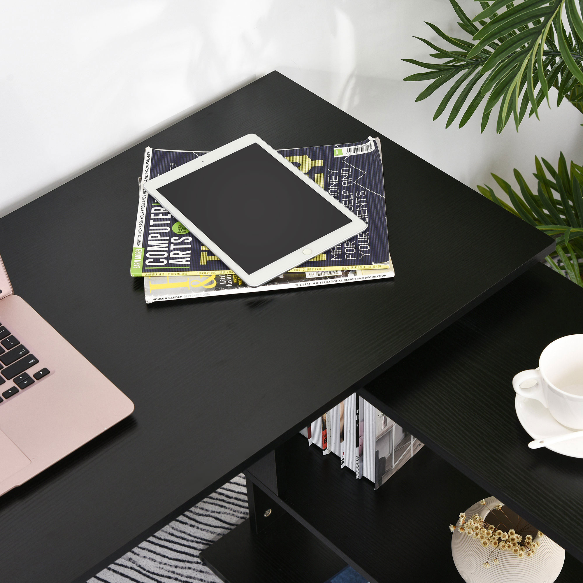 Un laptop oro rosa, tablet e riviste su una scrivania nera.