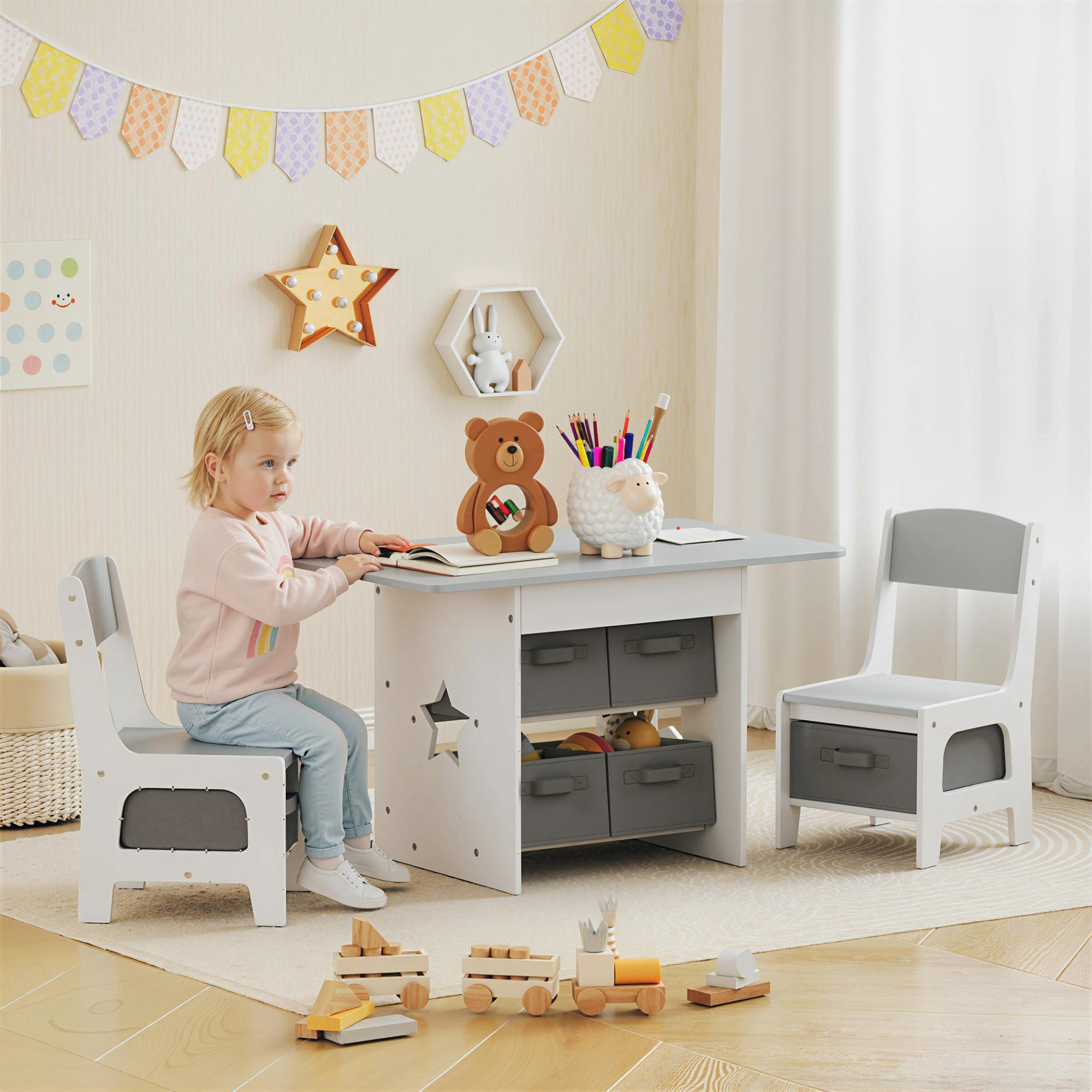 Una bambina siede a una scrivania con giocattoli, circondata da mobili per bambini.