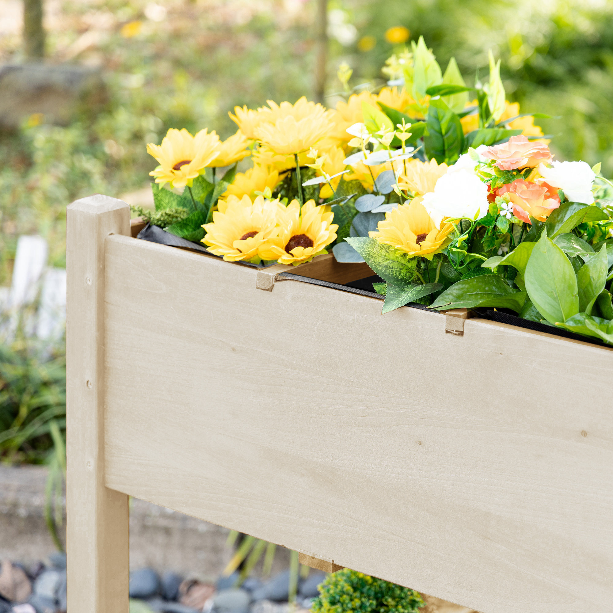 Una fioriera di legno piena di fiori gialli, arancioni e bianchi e foglie verdi.
