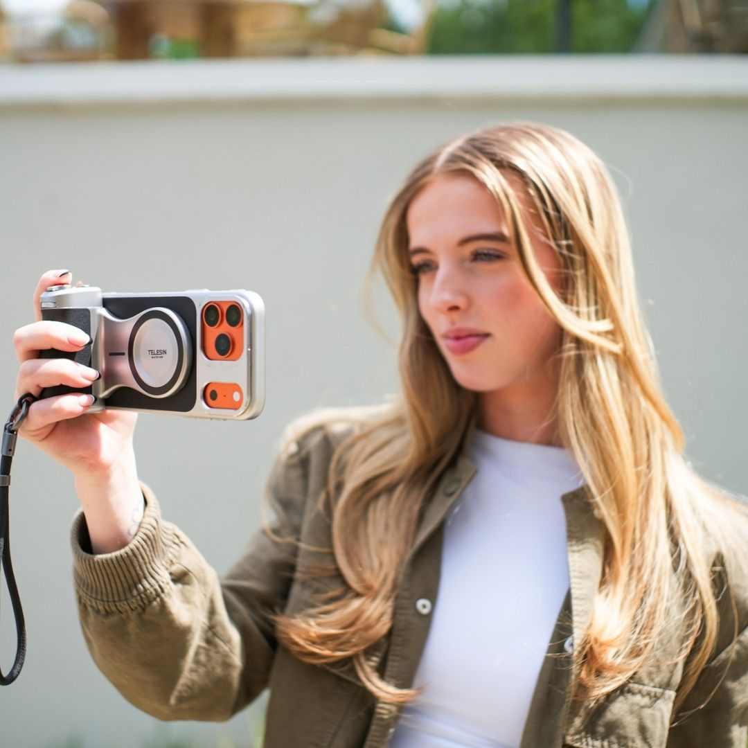 Een jonge vrouw houdt een camera vast. Ze draagt een olijfgroene jas.