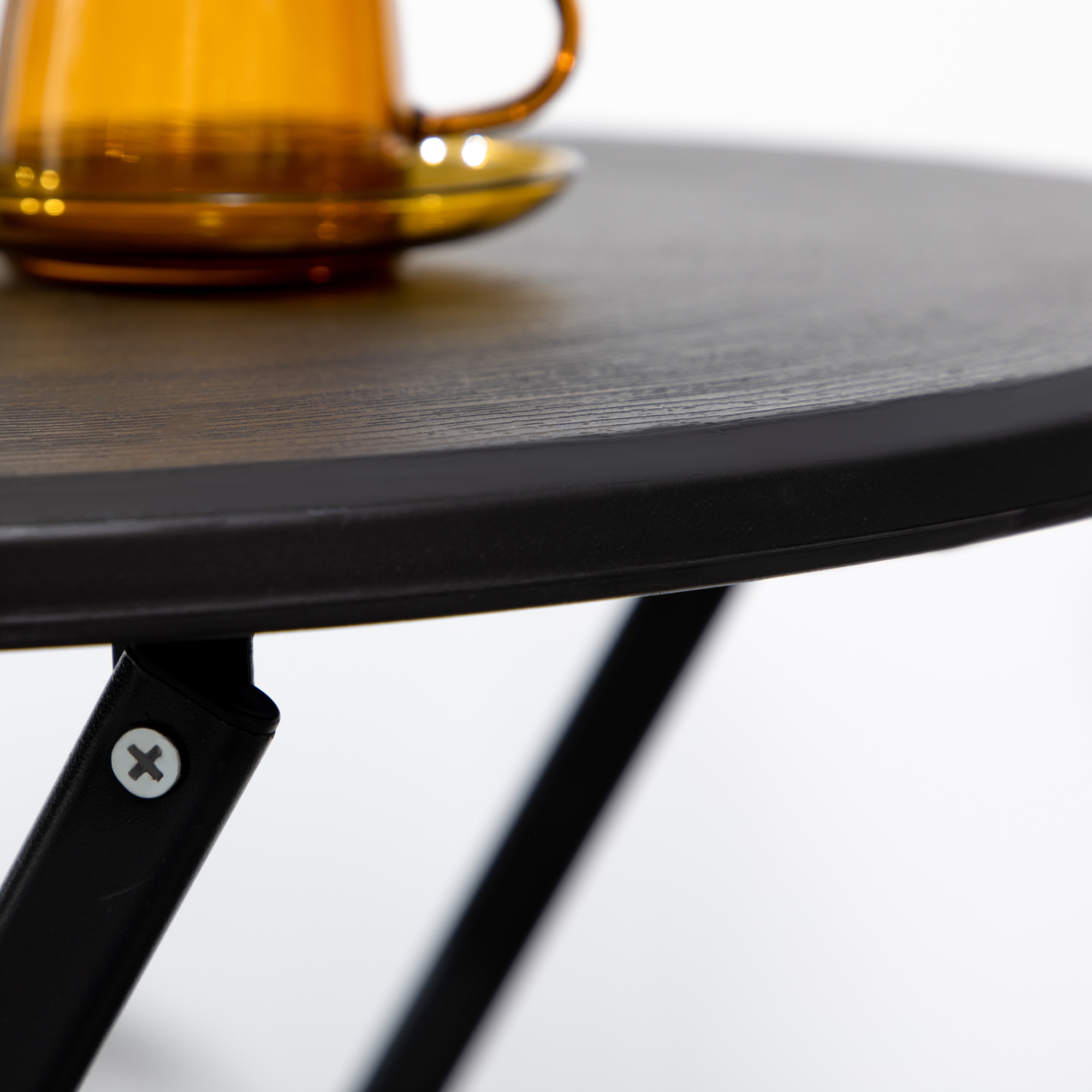 Tazza e piattino in vetro ambrato su tavolo in legno scuro con gambe in metallo nero.