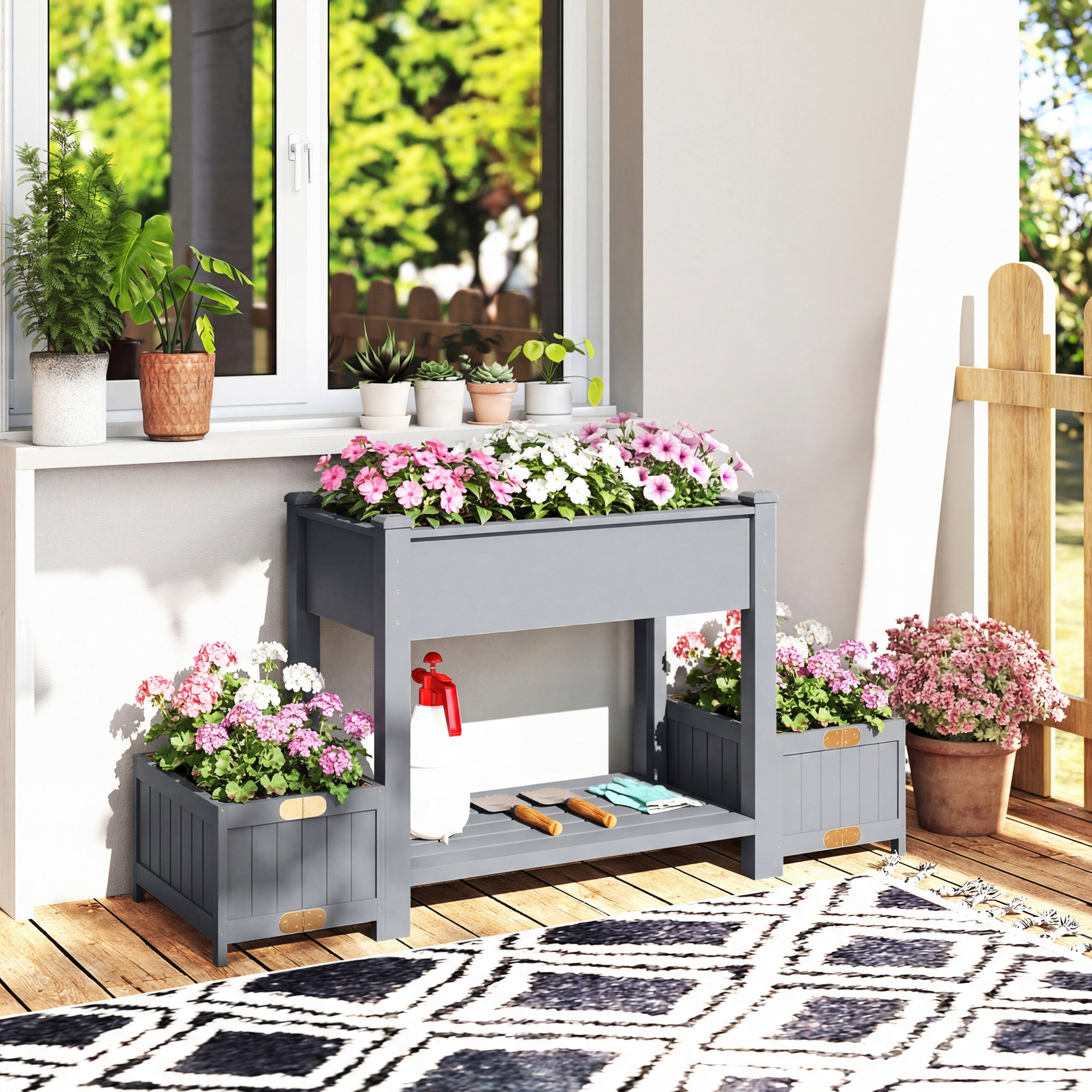 Un fioriera grigia a più livelli su un ponte di legno con fiori rosa e bianchi. Attrezzi da giardinaggio sul ripiano inferiore.