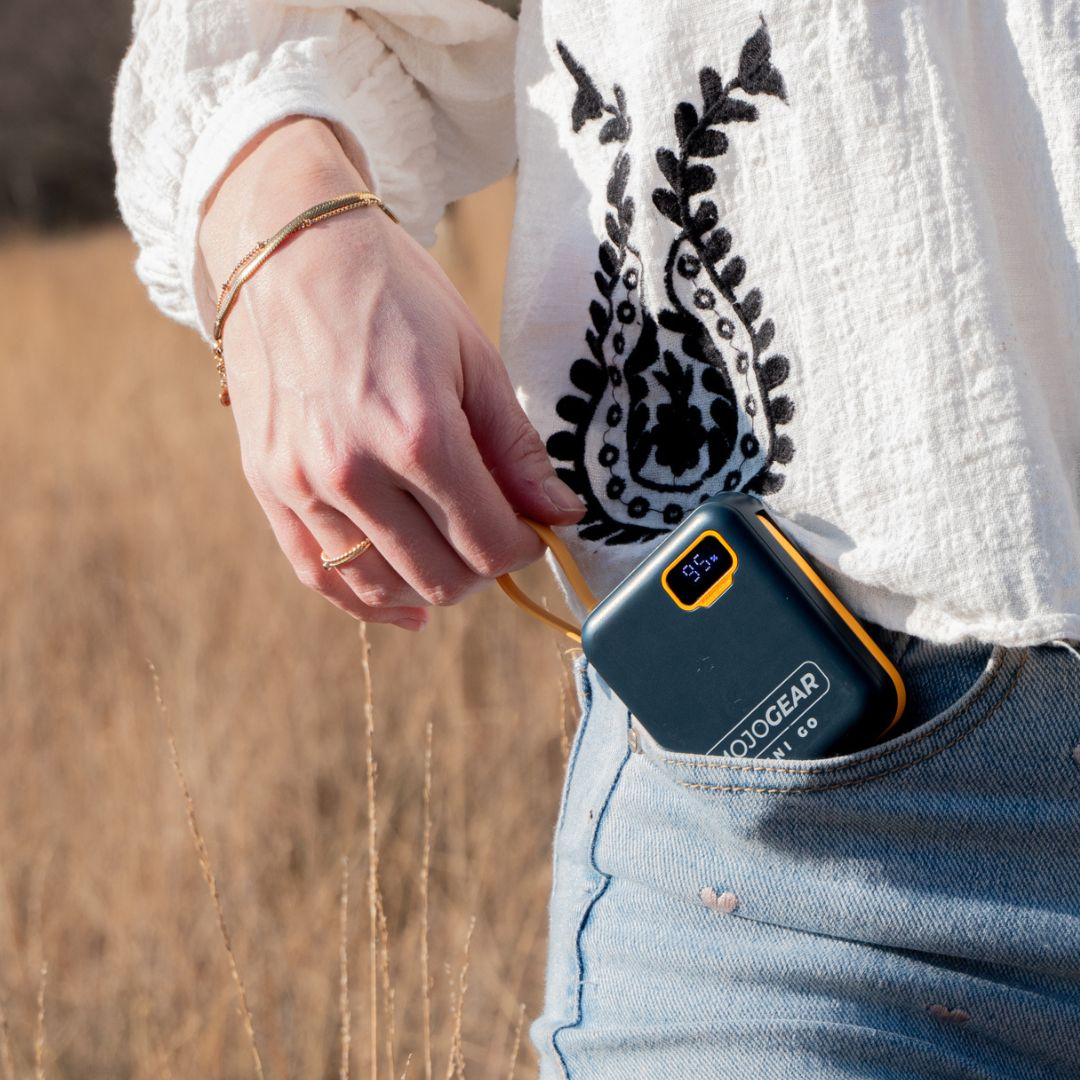 A hand places a dark blue power bank with yellow trim and a digital display into a denim pocket.