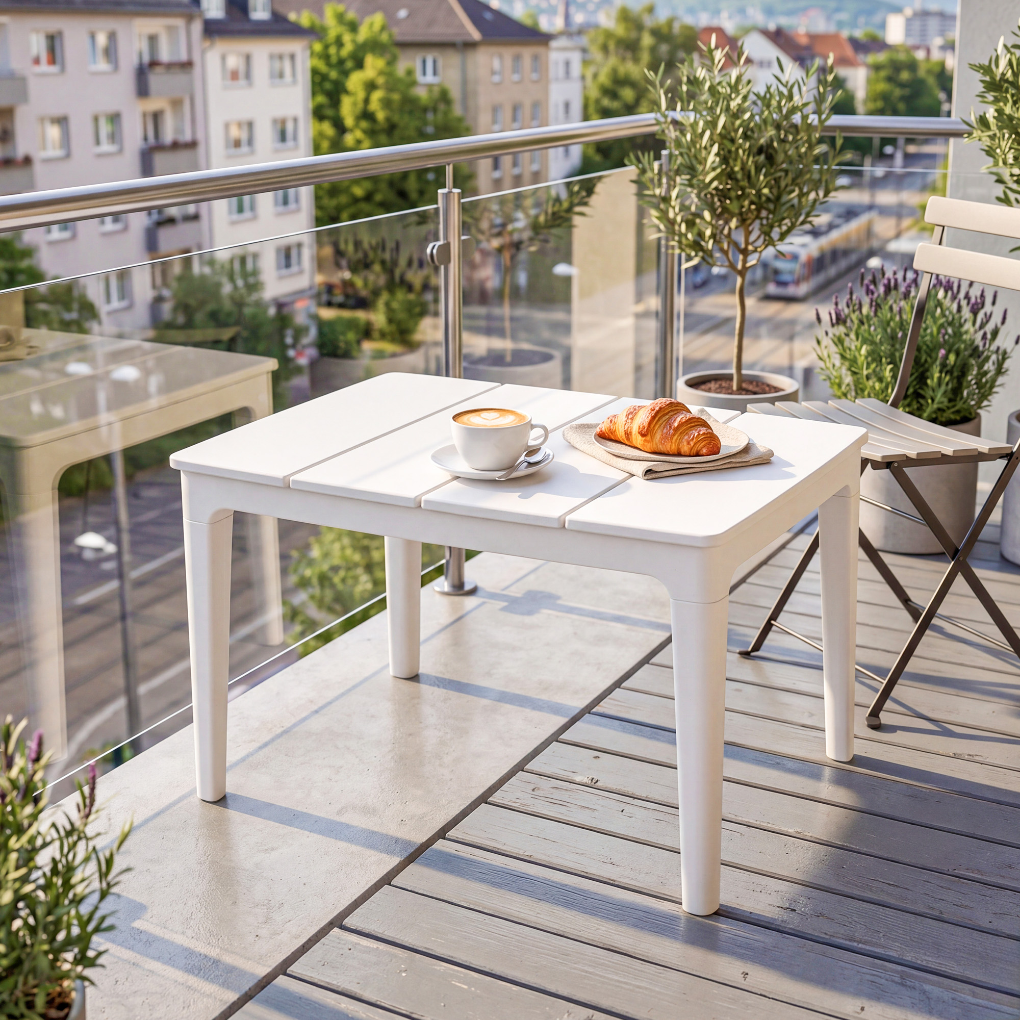 Tavolo bianco con caffè e croissant su balcone con piante e vista città.