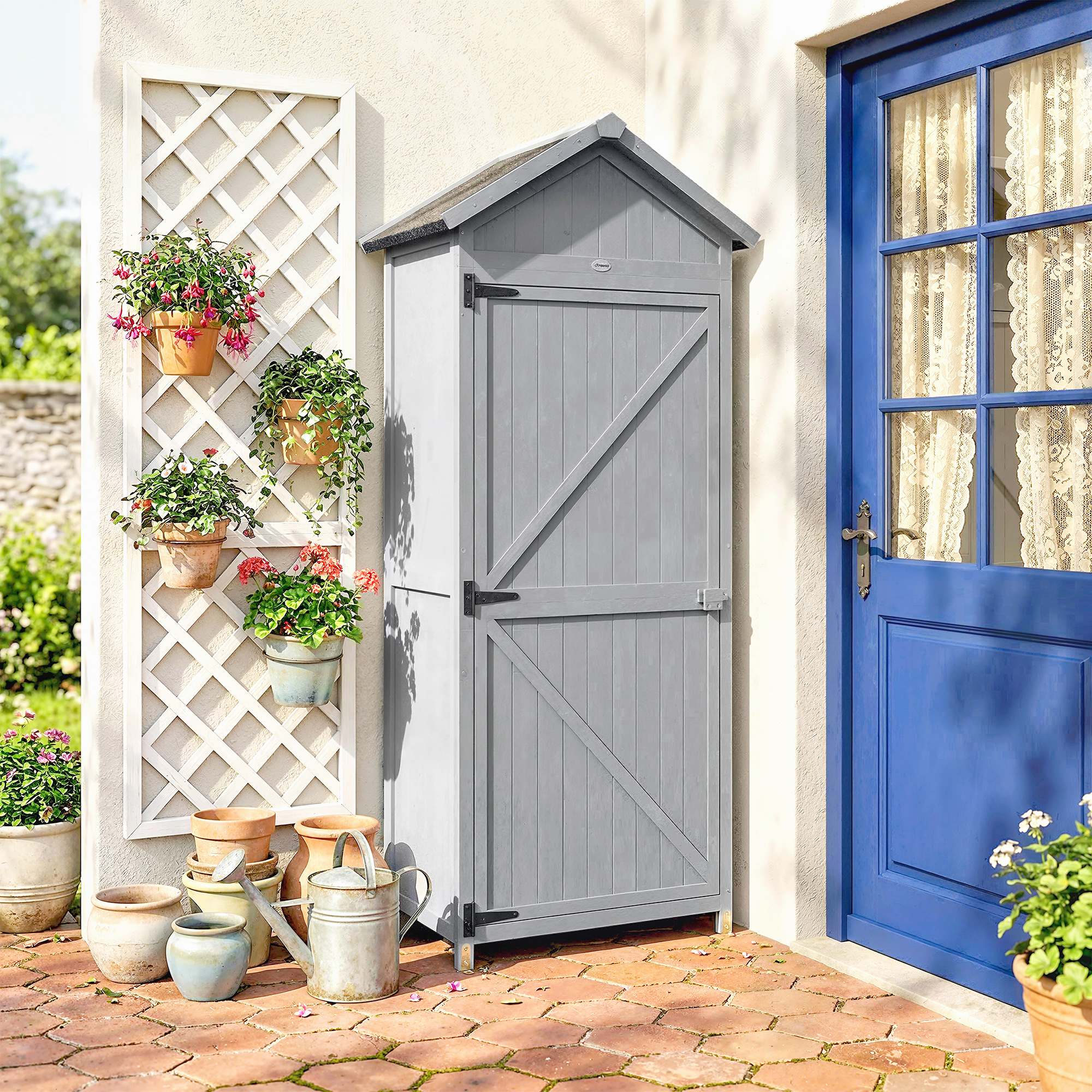 Capanno da giardino grigio accanto a porta blu, con piante su graticcio e vasi.