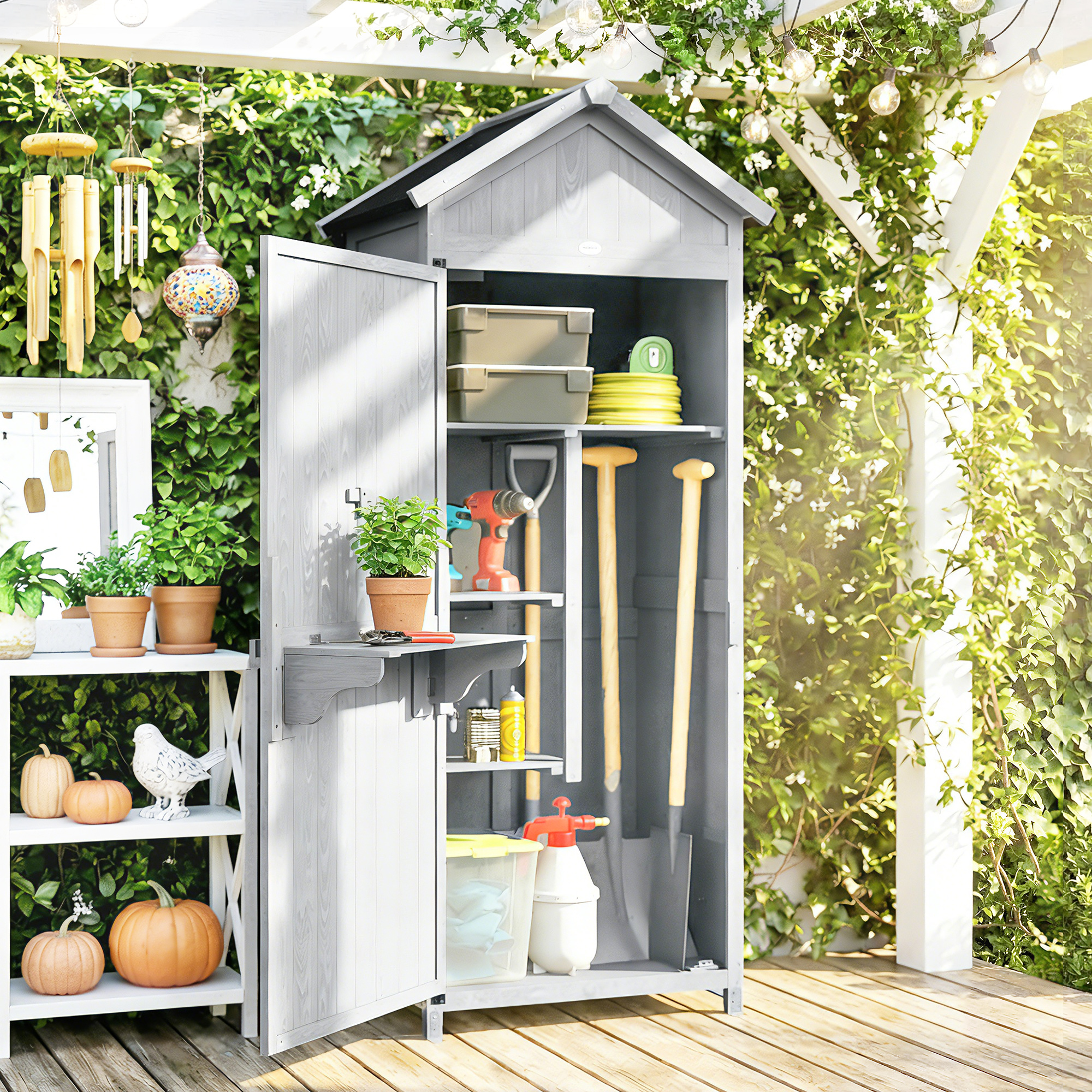 Un capanno da giardino grigio con attrezzi, piante e zucche accanto.