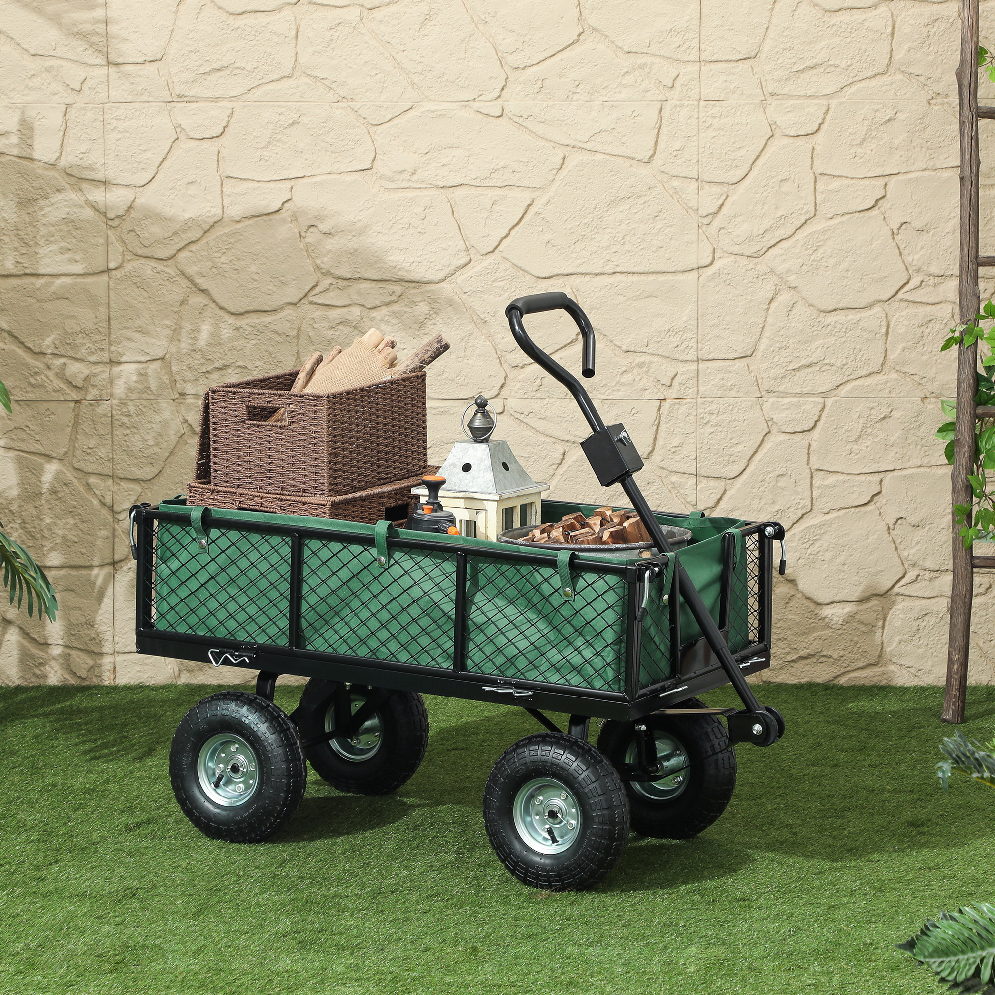 Un carrello da giardino verde con ruote, riempito di cesti, legna e lanterne su erba sintetica.