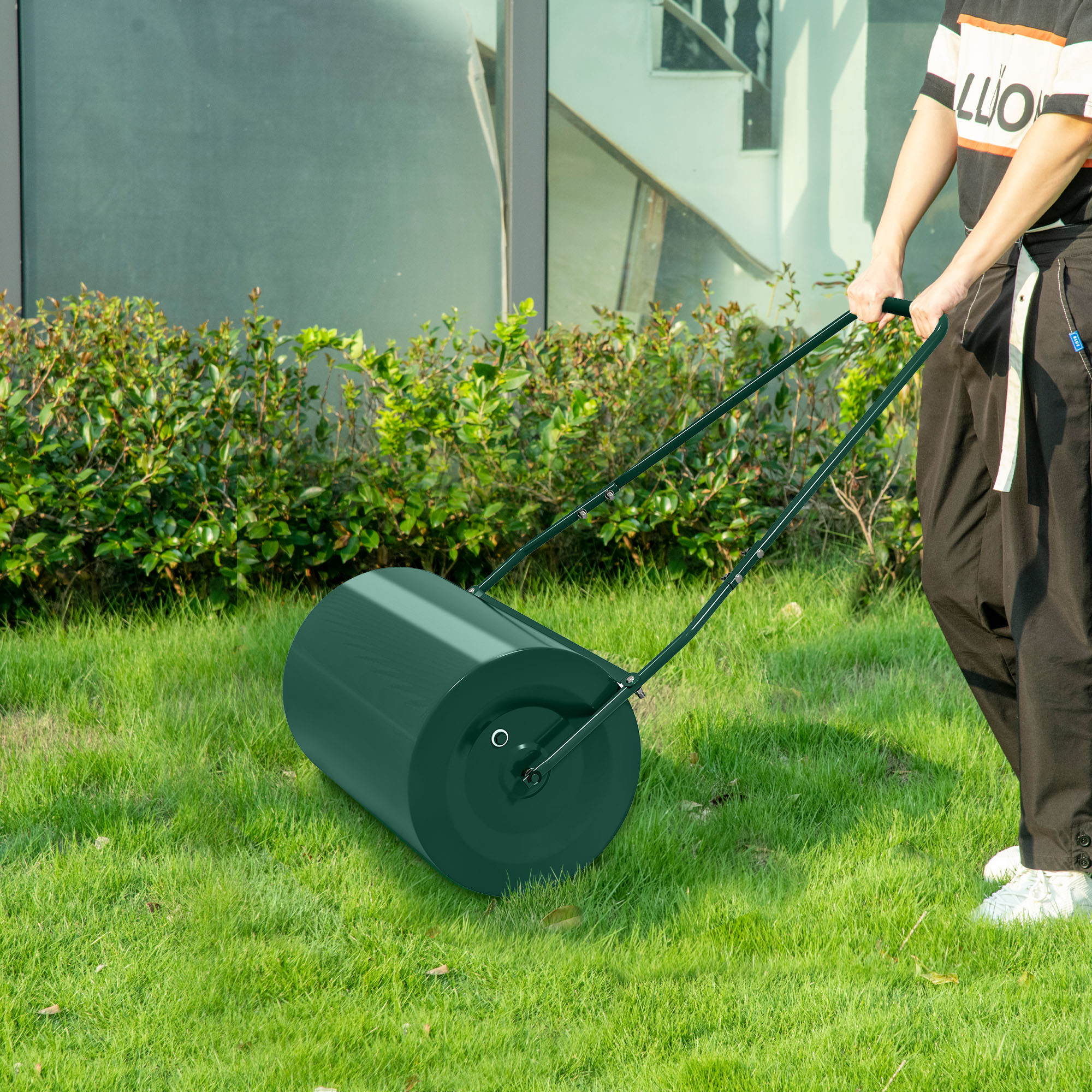 Persona che spinge un rullo da prato verde sull'erba accanto a cespugli.