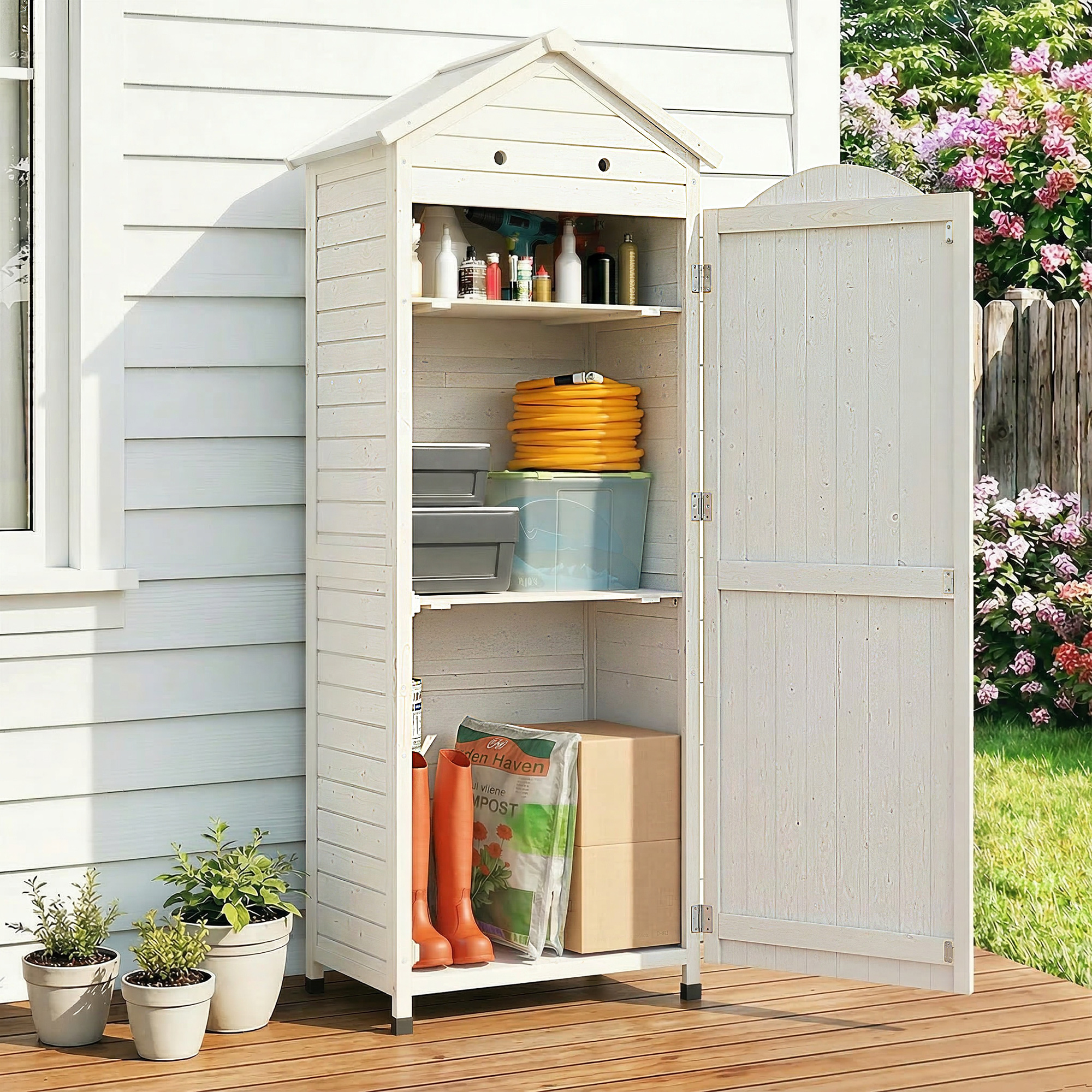 Un capanno da giardino bianco con porta aperta, riempito con attrezzi, piante e scatole.