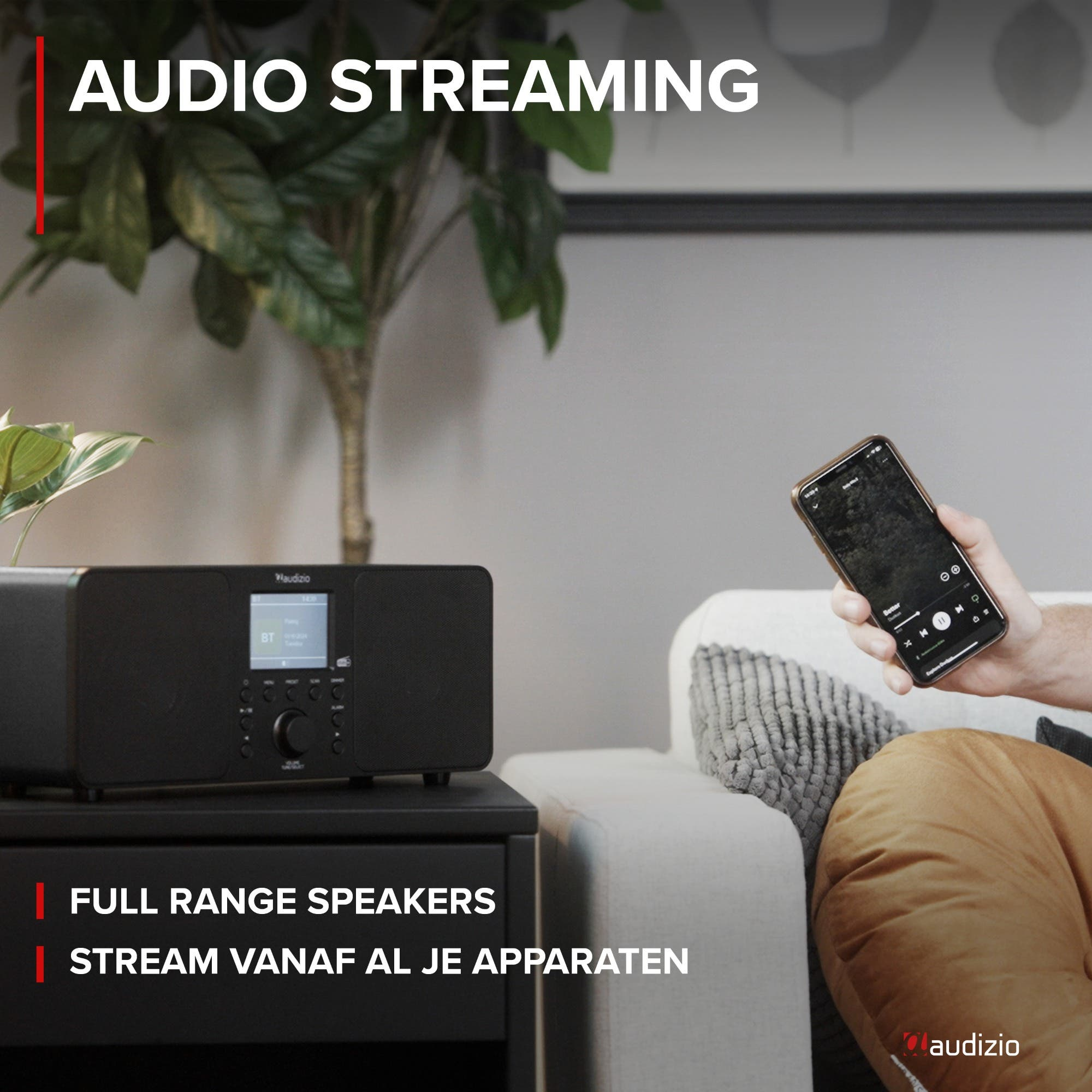 Ein schwarzes Audizio-Radio steht neben einer Pflanze. Ein Mann hält ein Smartphone in der Hand.