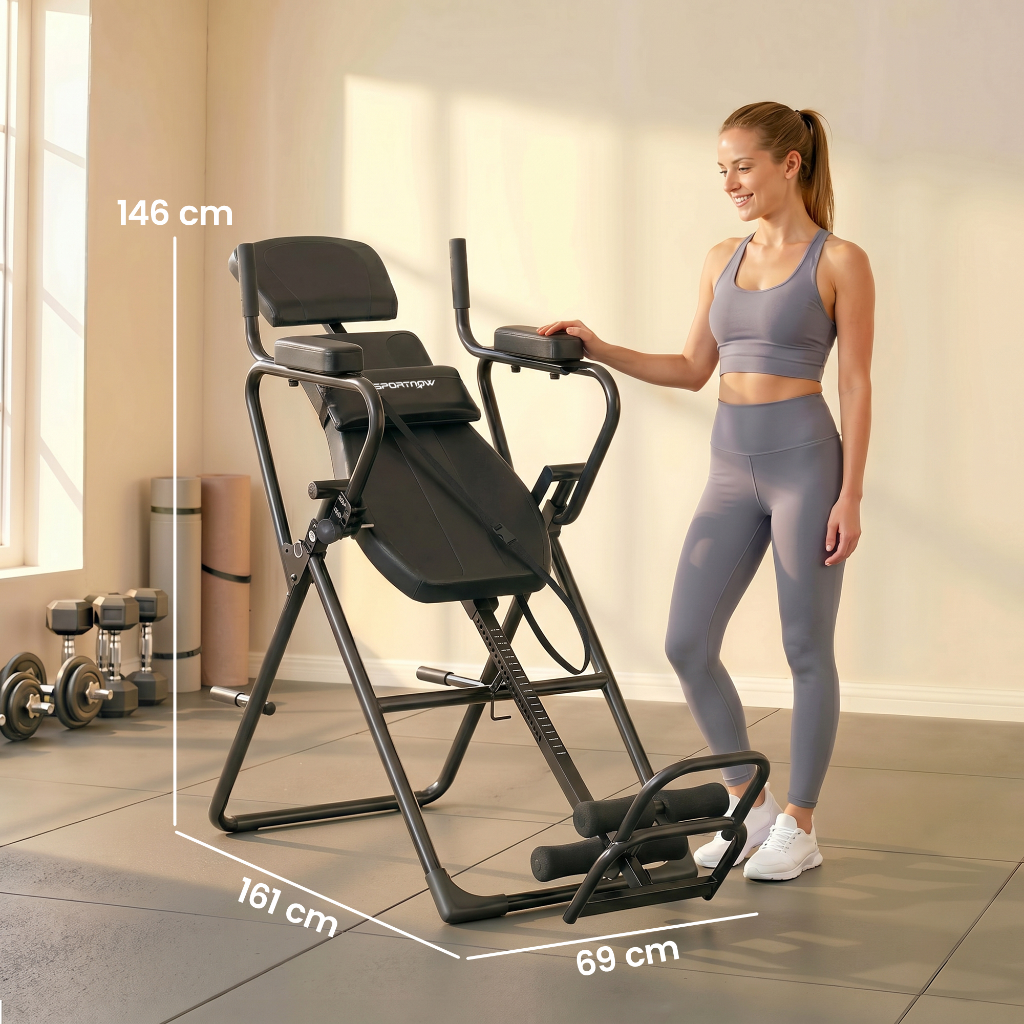 Una donna accanto a una macchina per inversioni nera in palestra. Vengono mostrate le dimensioni.