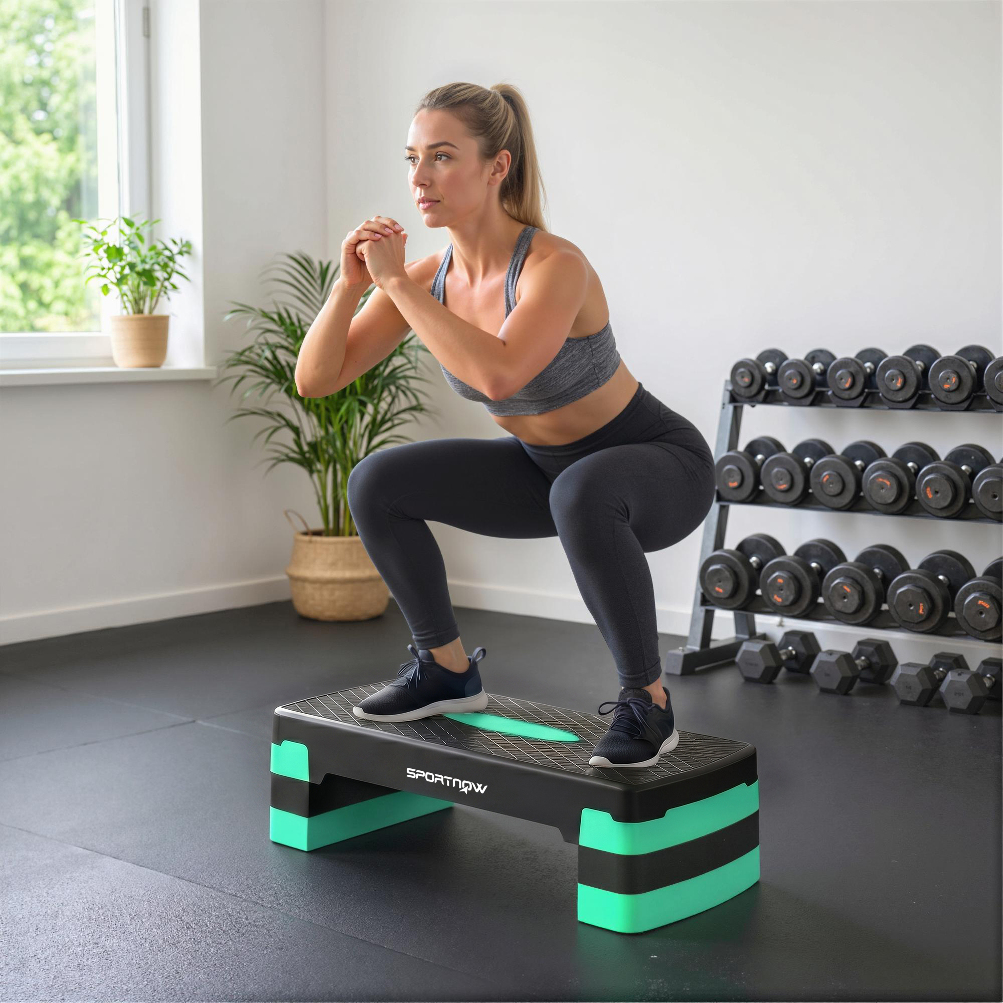 Donna esegue squat su una scatola fitness nera e verde con manubri sullo sfondo.