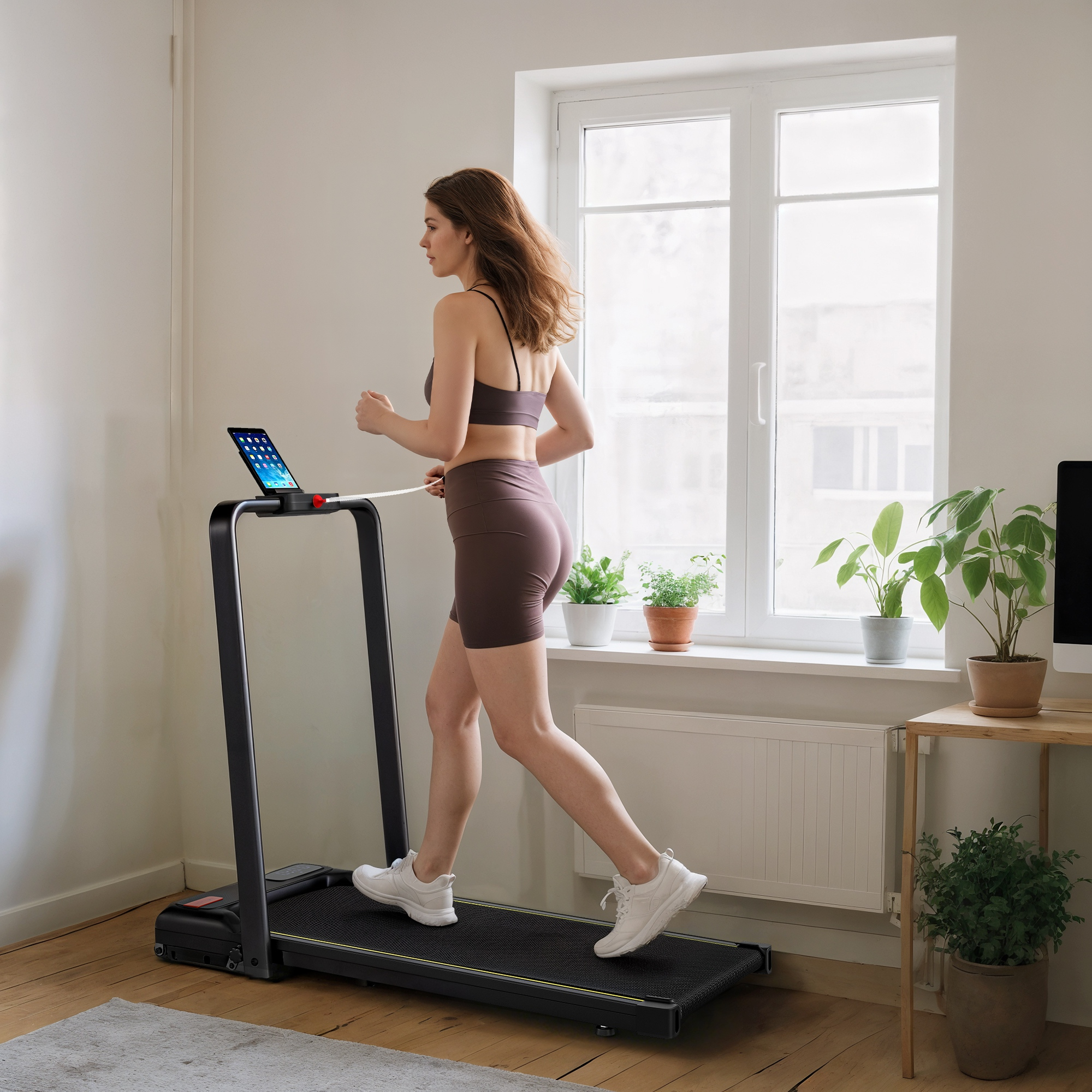 Donna corre su tapis roulant con tablet, piante vicino finestra.