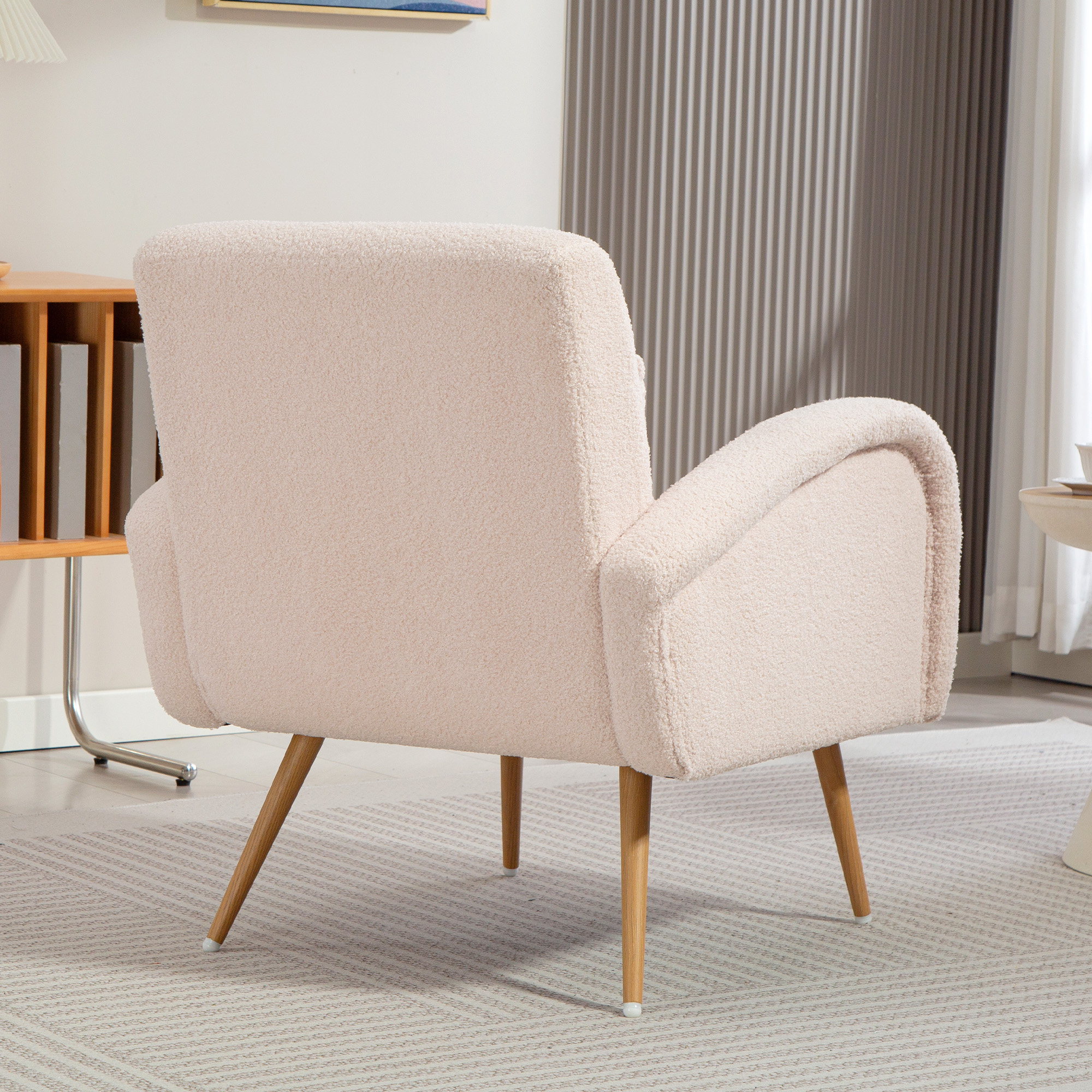 Una poltrona bouclé color crema con gambe in legno poggia su un tappeto a motivi.