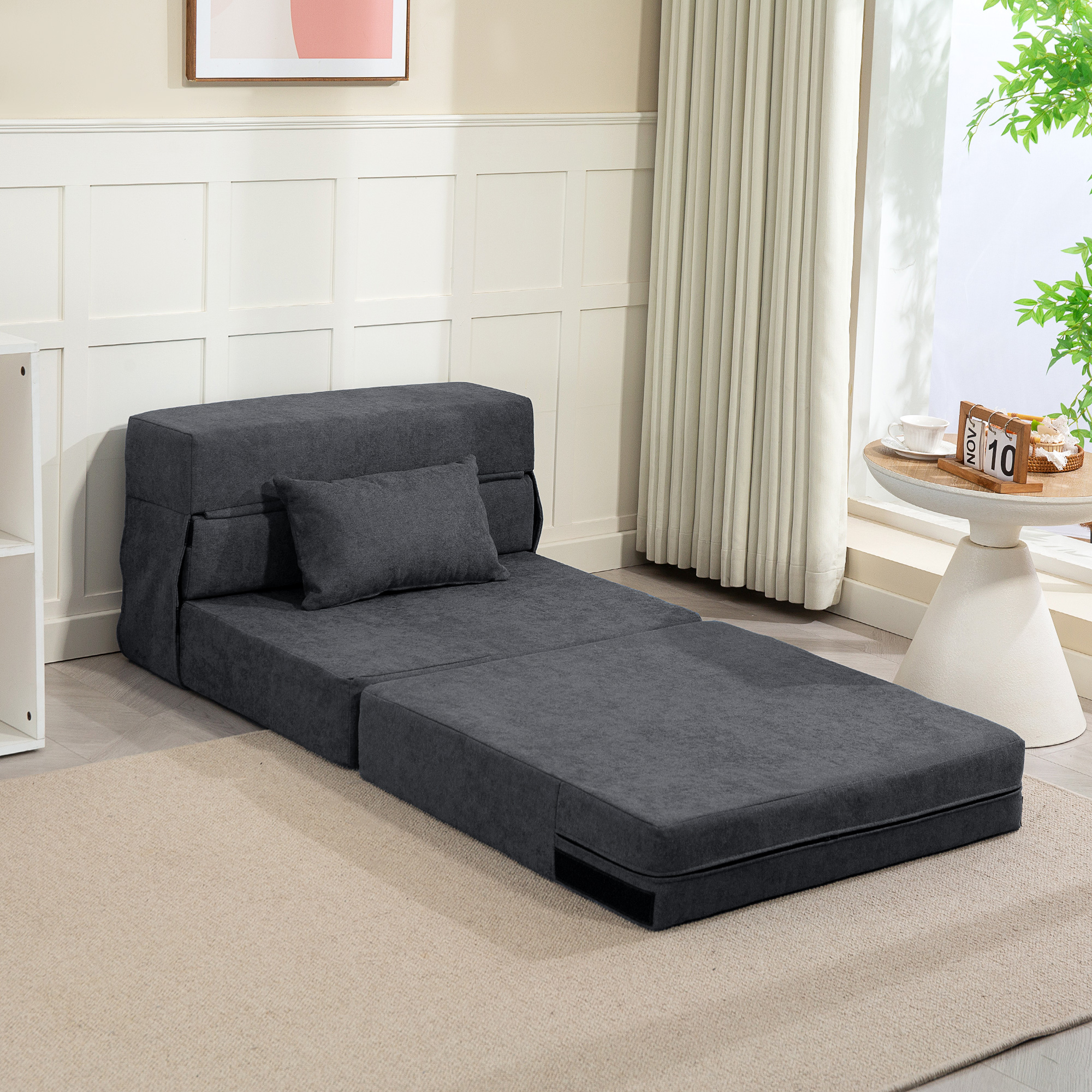 Un divano letto grigio scuro con cuscino, aperto su tappeto beige.