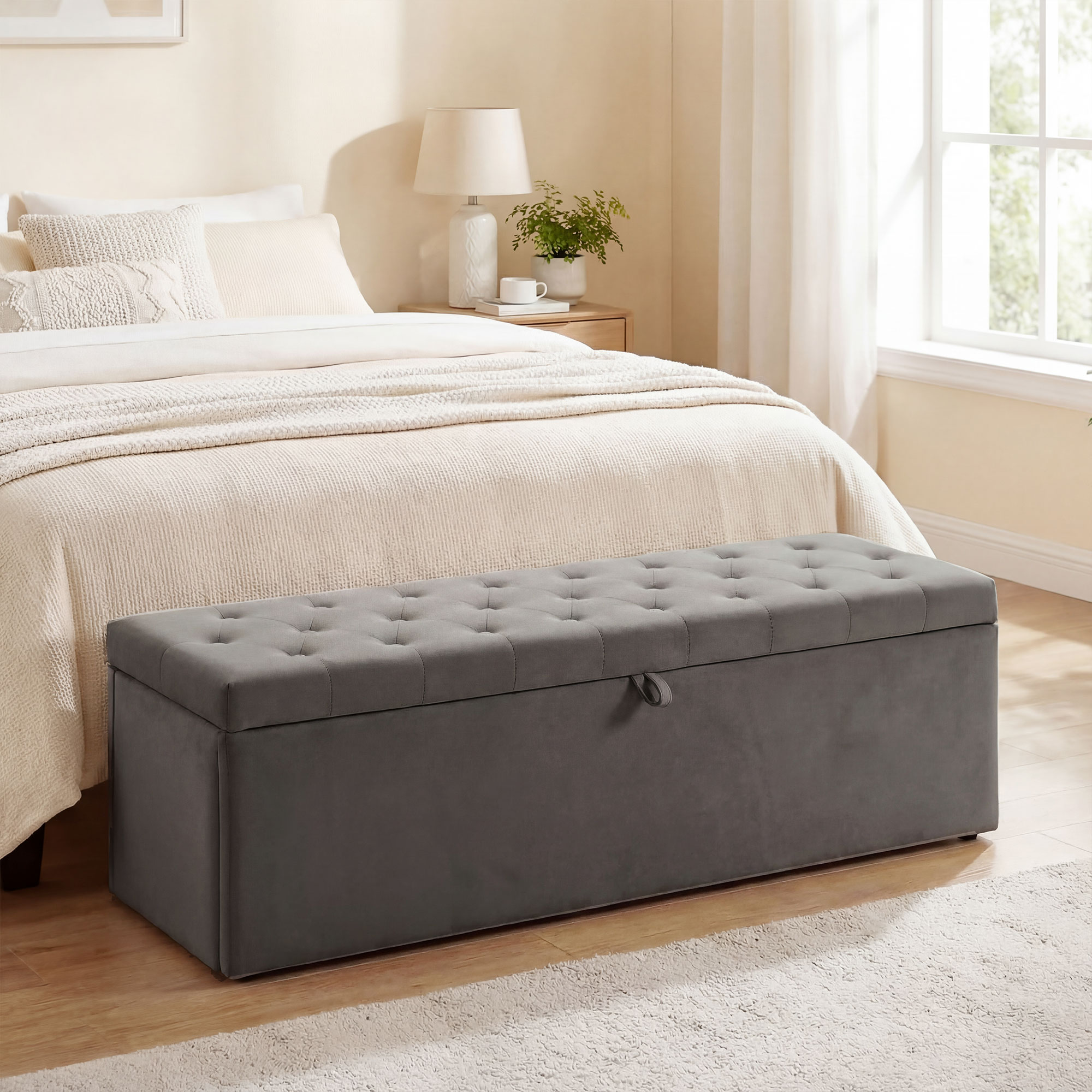 Un pouf contenitore grigio trapuntato è posizionato davanti a un letto.